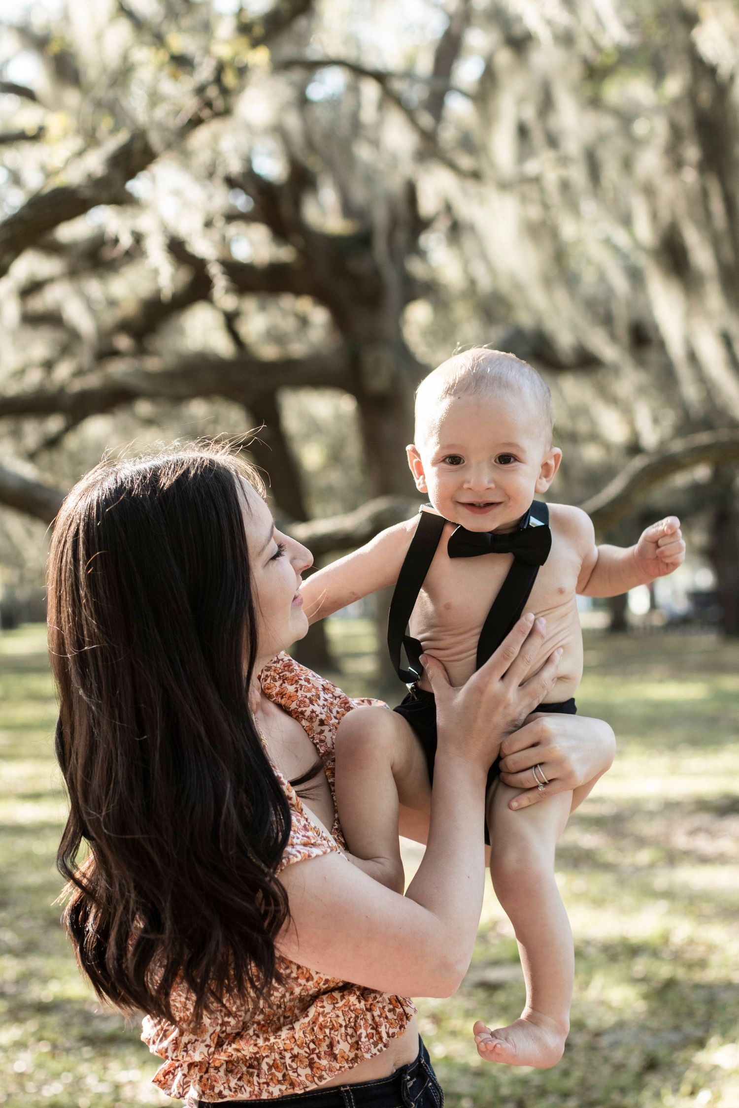 Mother and baby share playful moments outdoors surrounded by trees.