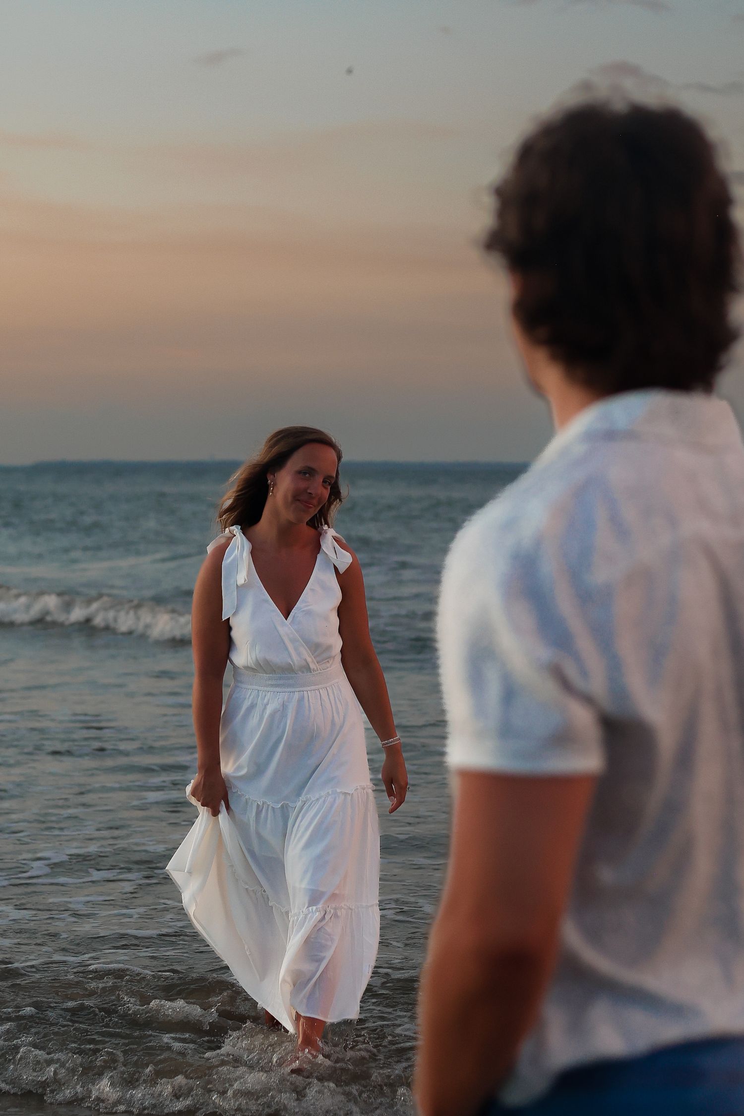 Couple enjoying a romantic moment along the shoreline at sunset with waves lapping at their feet.
