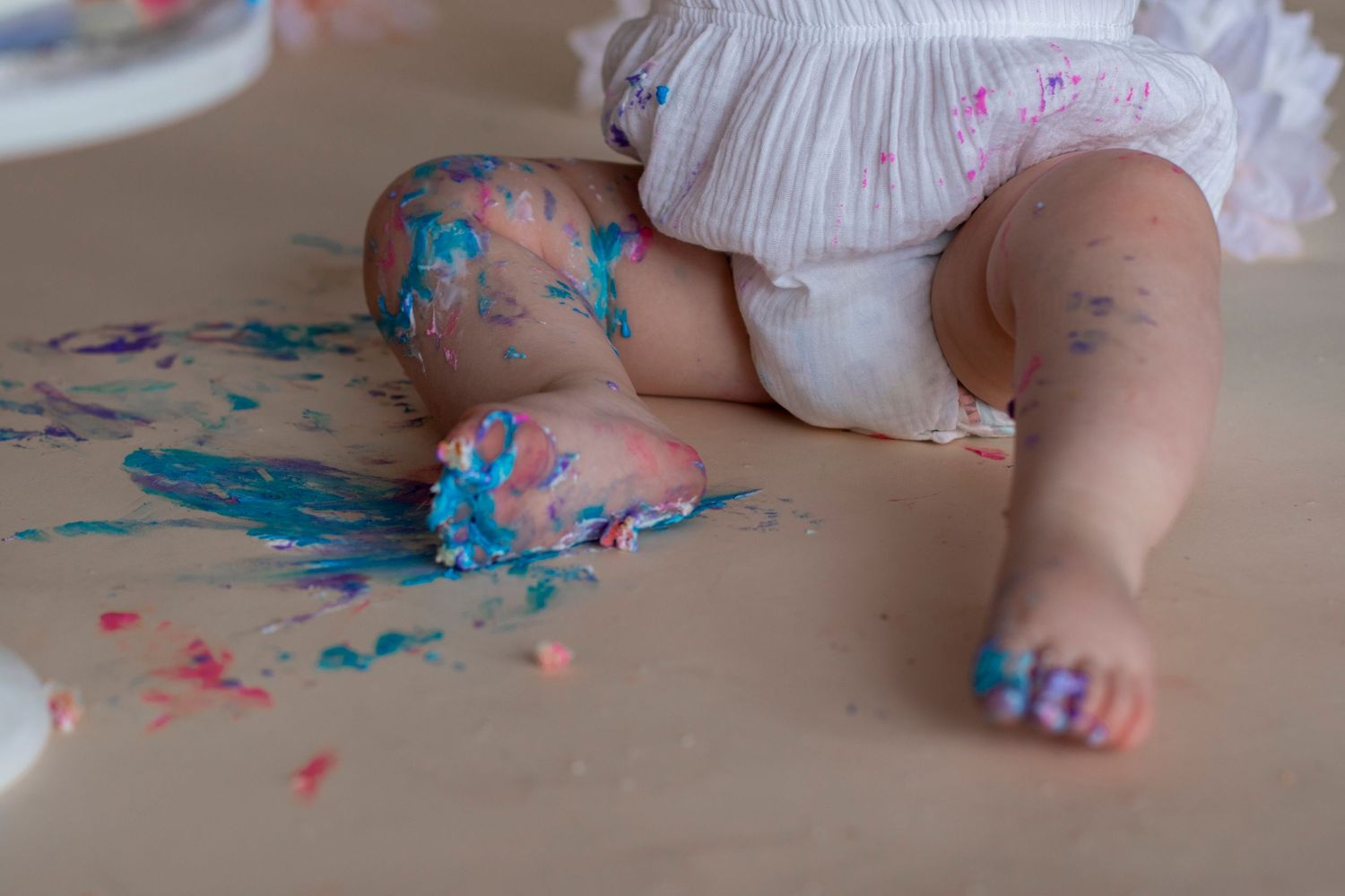 Close-up of tiny feet and cake smash mess with pink and blue frosting on the floor.