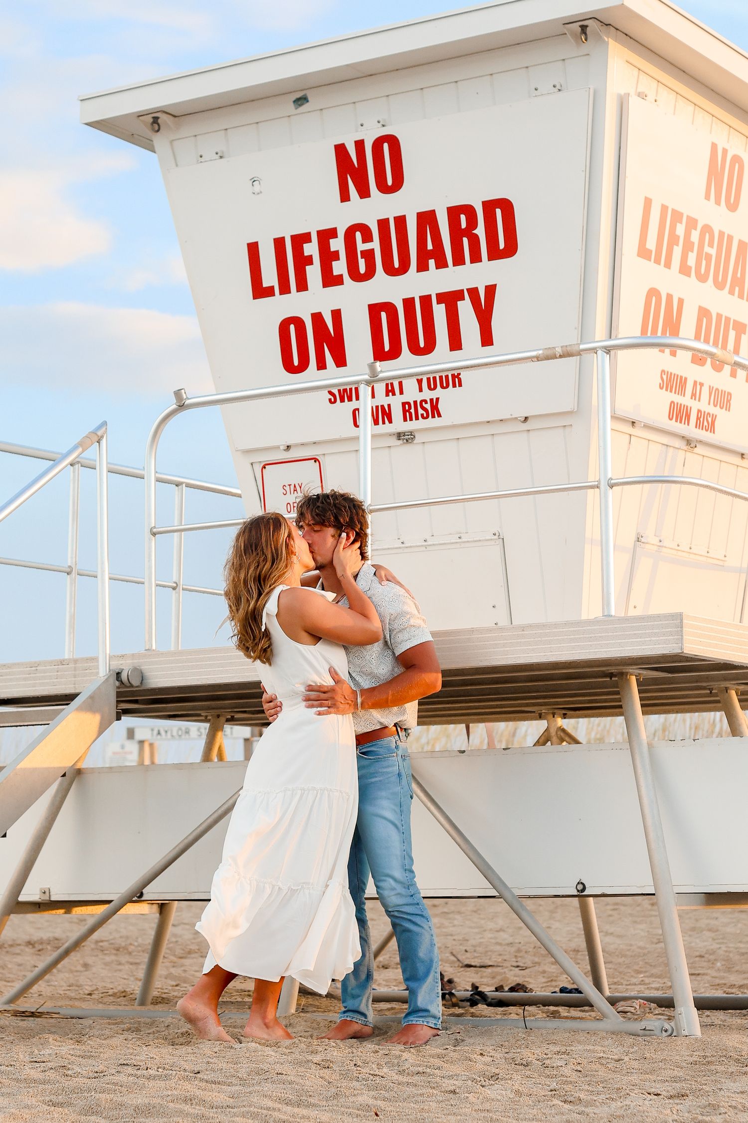 Couple sharing romantic moment by lifeguard tower on beach at sunset.