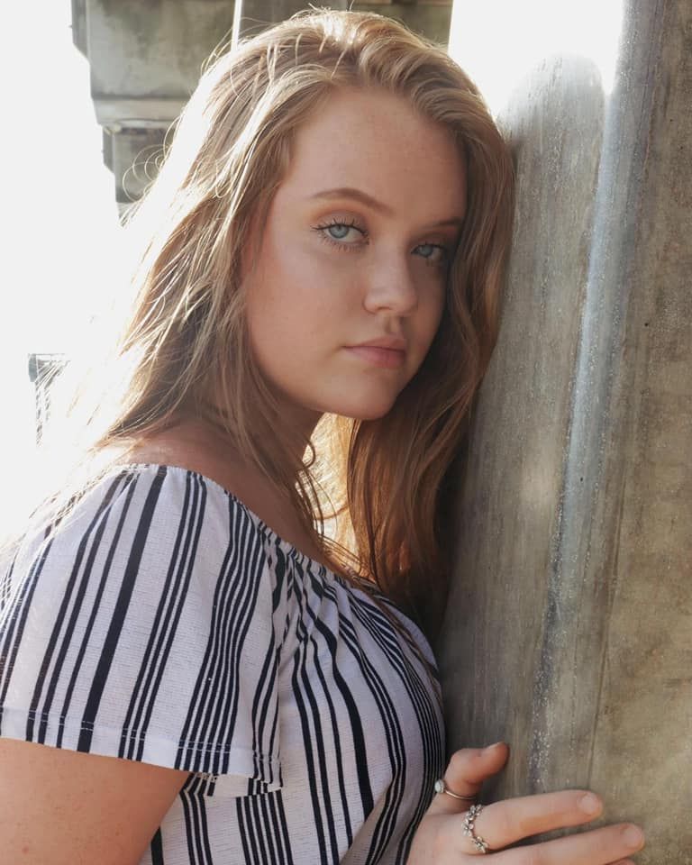 Artistic portrait against stone column with dramatic side lighting.
