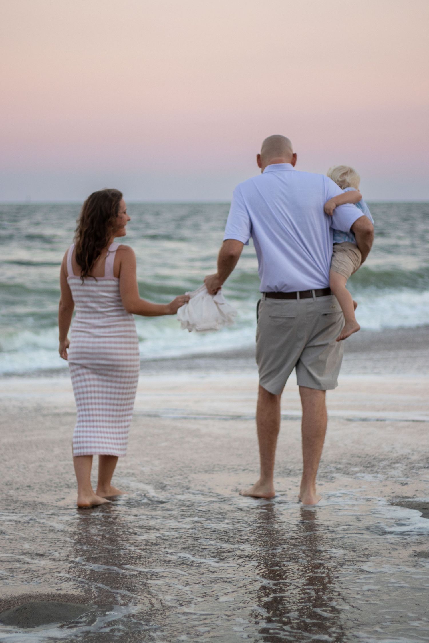 A family walks along the shoreline at sunset with waves rolling in.