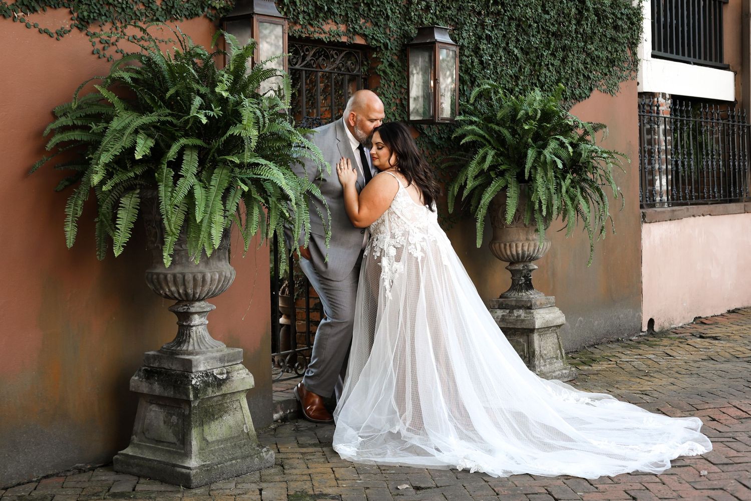 Wedding portraits against an ivy-covered wall with elegant urns and garden decor.