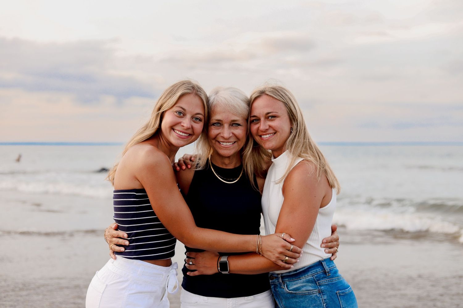 Three friends share joyful embraces and laughter while enjoying a sunny day at the beach.