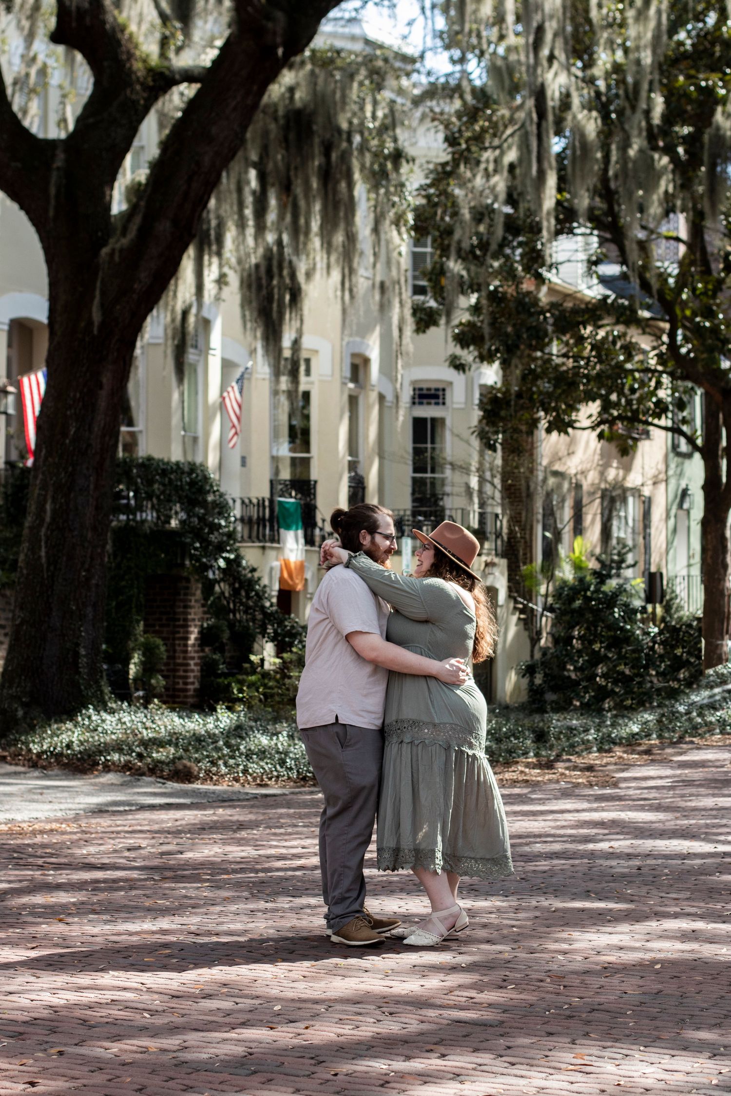 Spanish moss hangs from trees along a brick pathway near historic buildings.