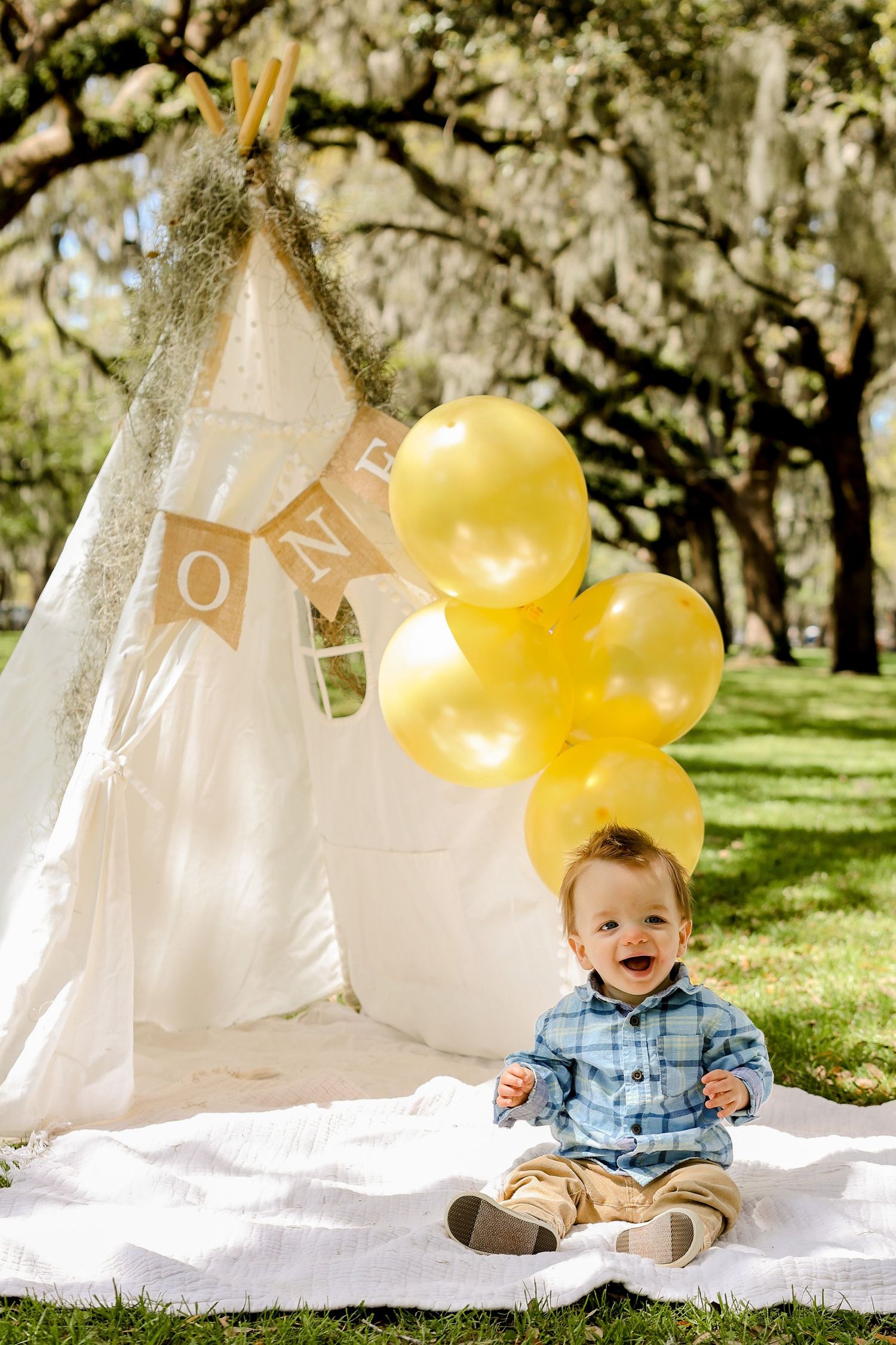 Outdoor first birthday setup with white teepee, yellow balloons and ONE banner.