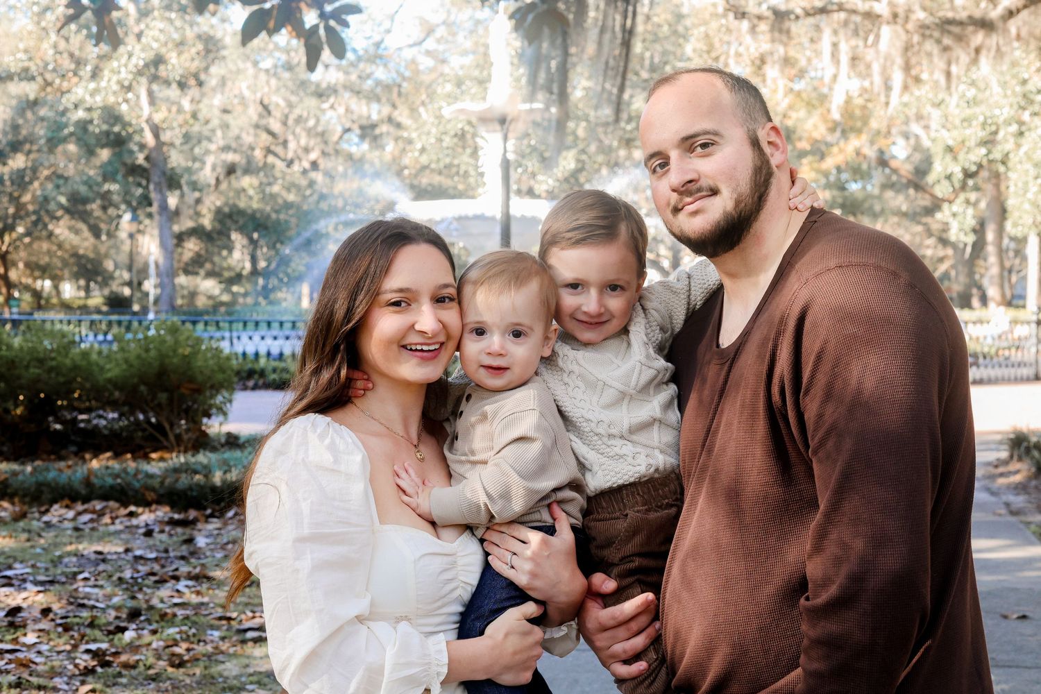 A family group poses together outdoors during autumn surrounded by trees.