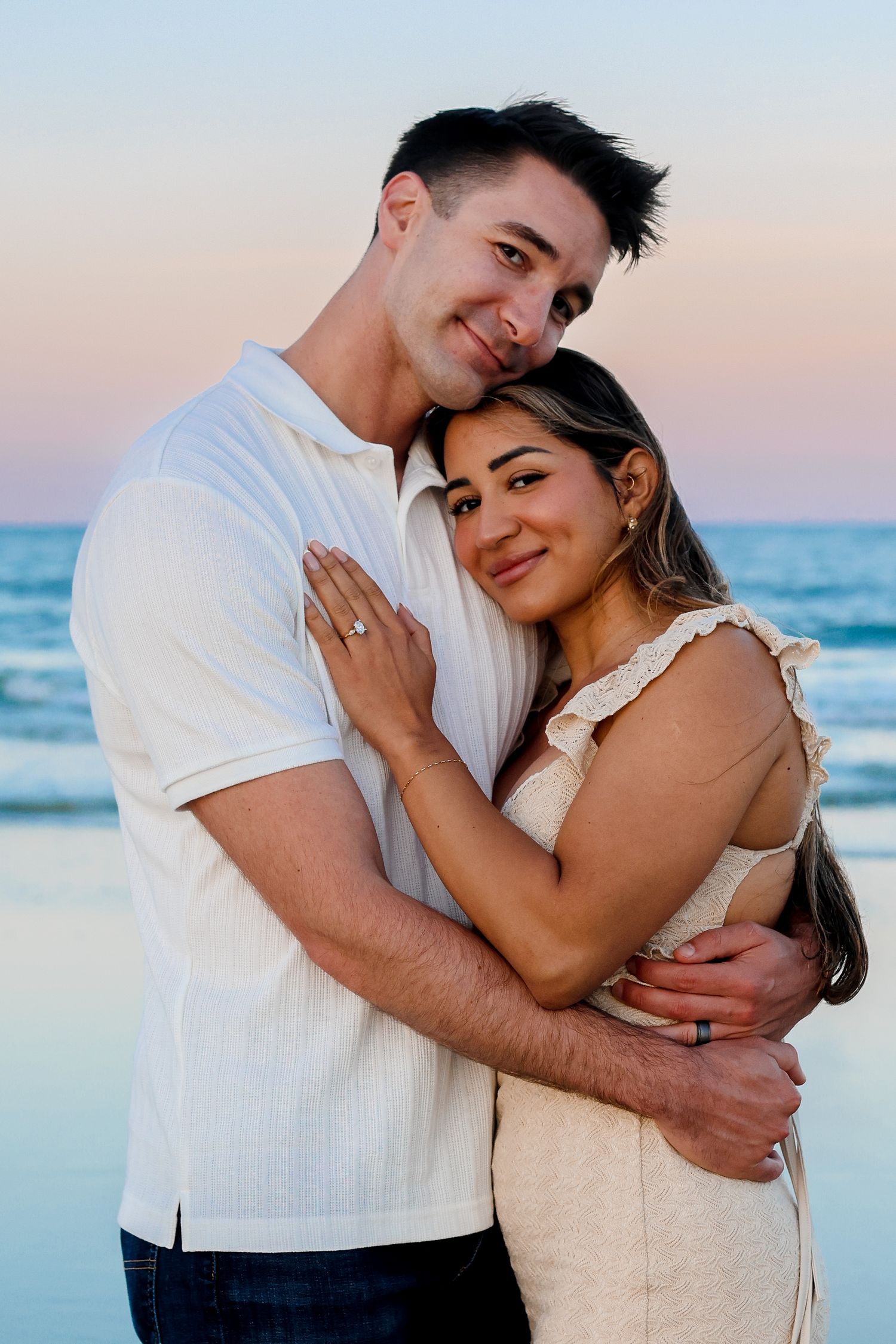 Romantic beach engagement photo with ocean waves in background during sunset.