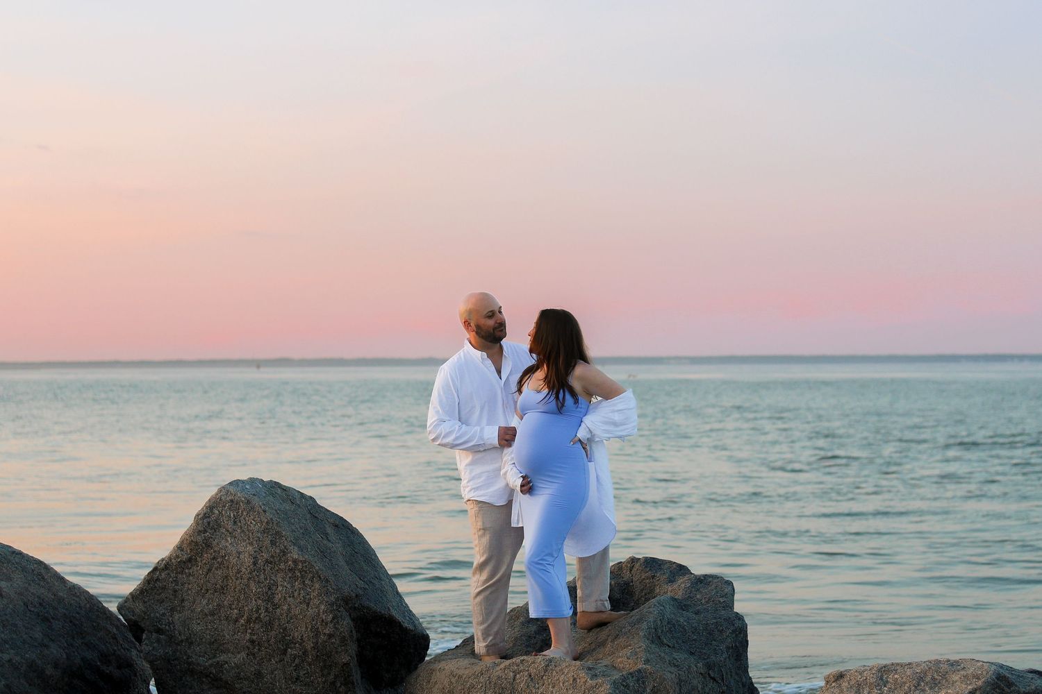 A couple sharing intimate moments on rocky beach formations during golden hour.