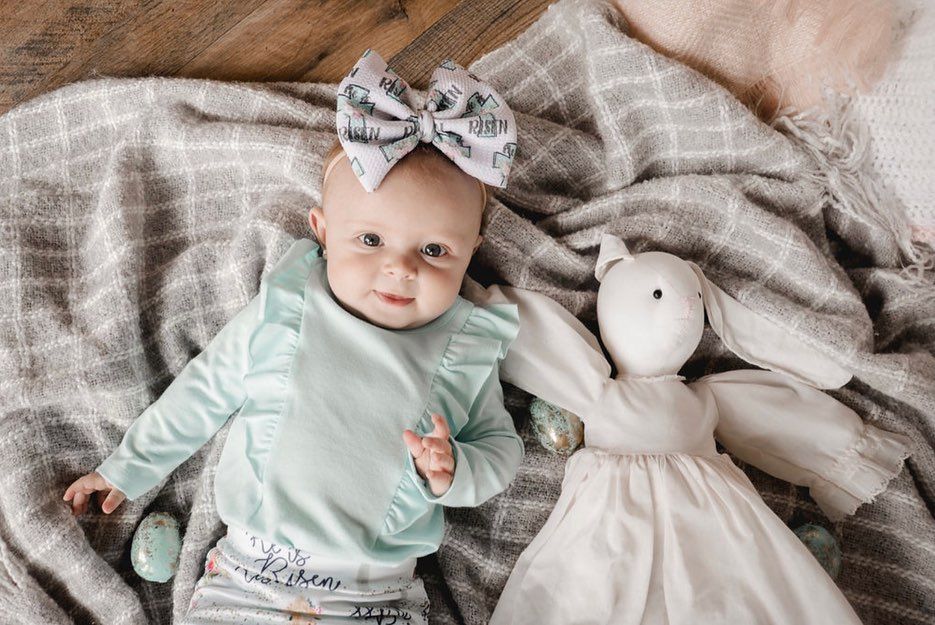 Mint green outfit and striped bow accessory with plush bunny toy on gray blanket.