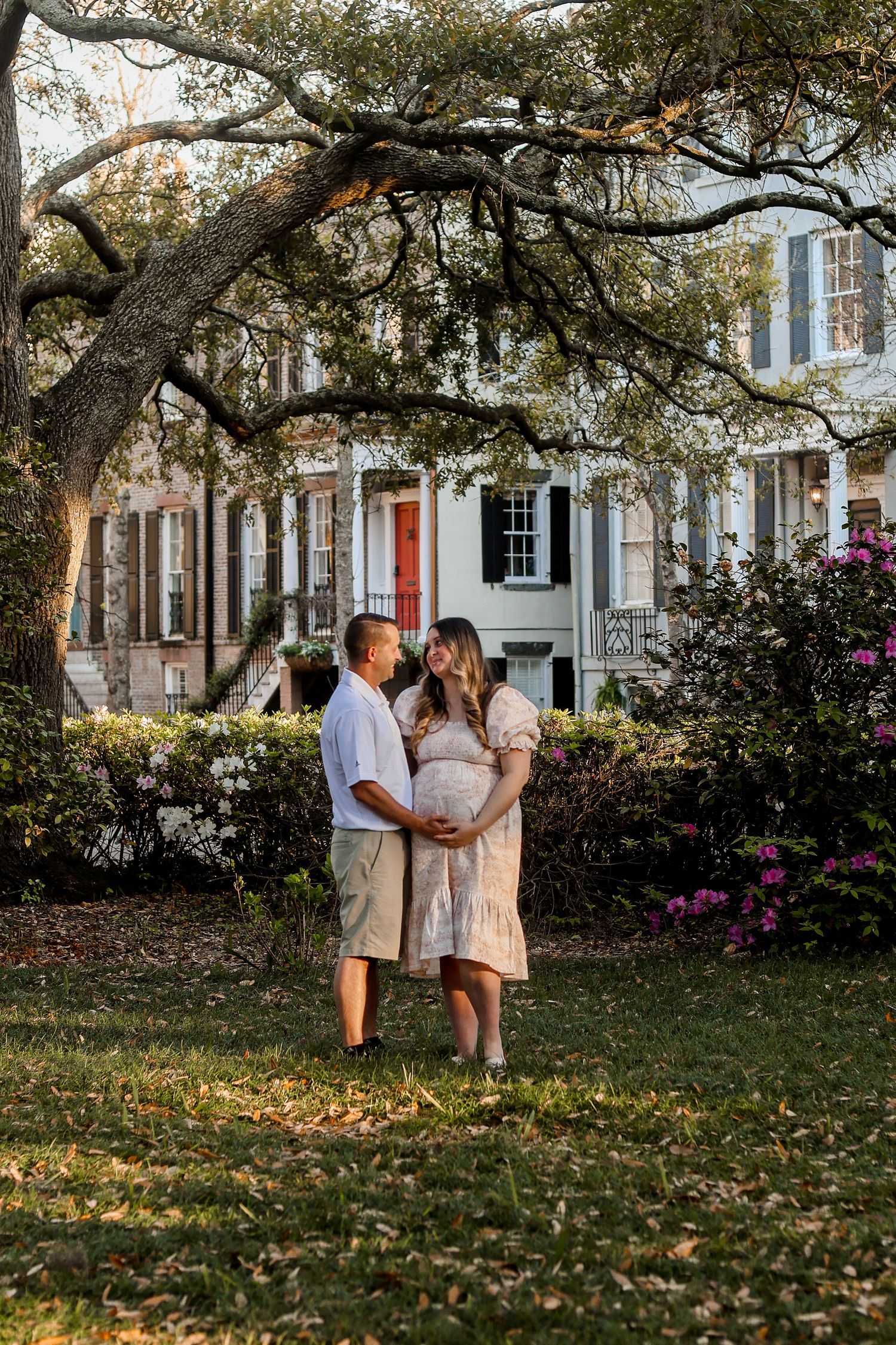 A couple sharing an intimate moment under oak trees in front of a historic home.