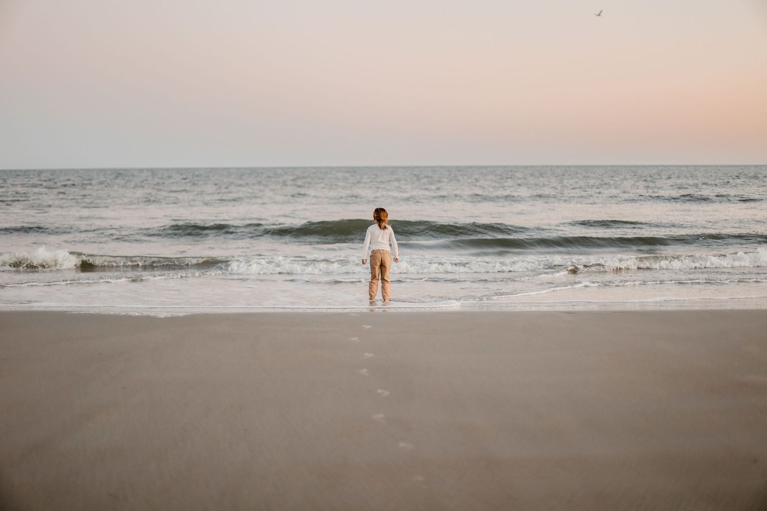 A tranquil sunset beach scene with gentle waves rolling onto the sand under warm evening light.