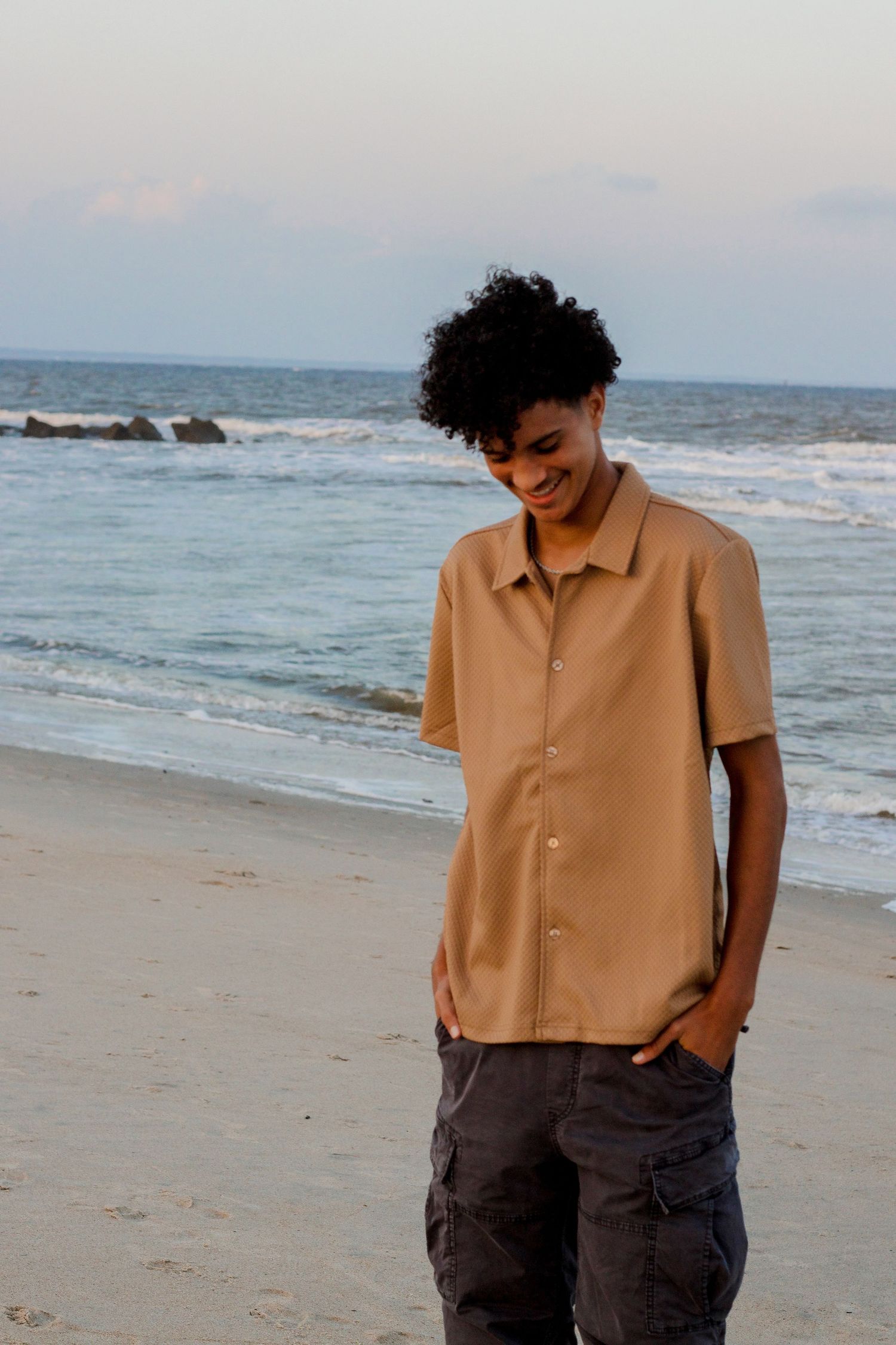 Casual beachside portrait with ocean waves and rocks in background.