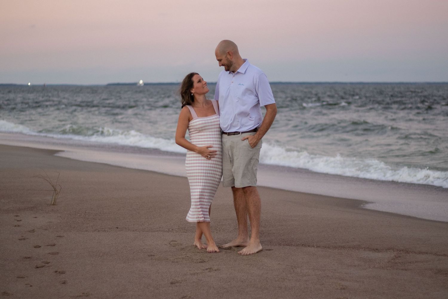 Several couples walk along the shoreline during sunset with waves lapping at the sand.