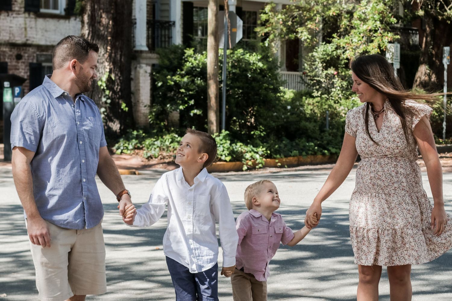 Family walking together on a tree-lined sidewalk on a sunny day.