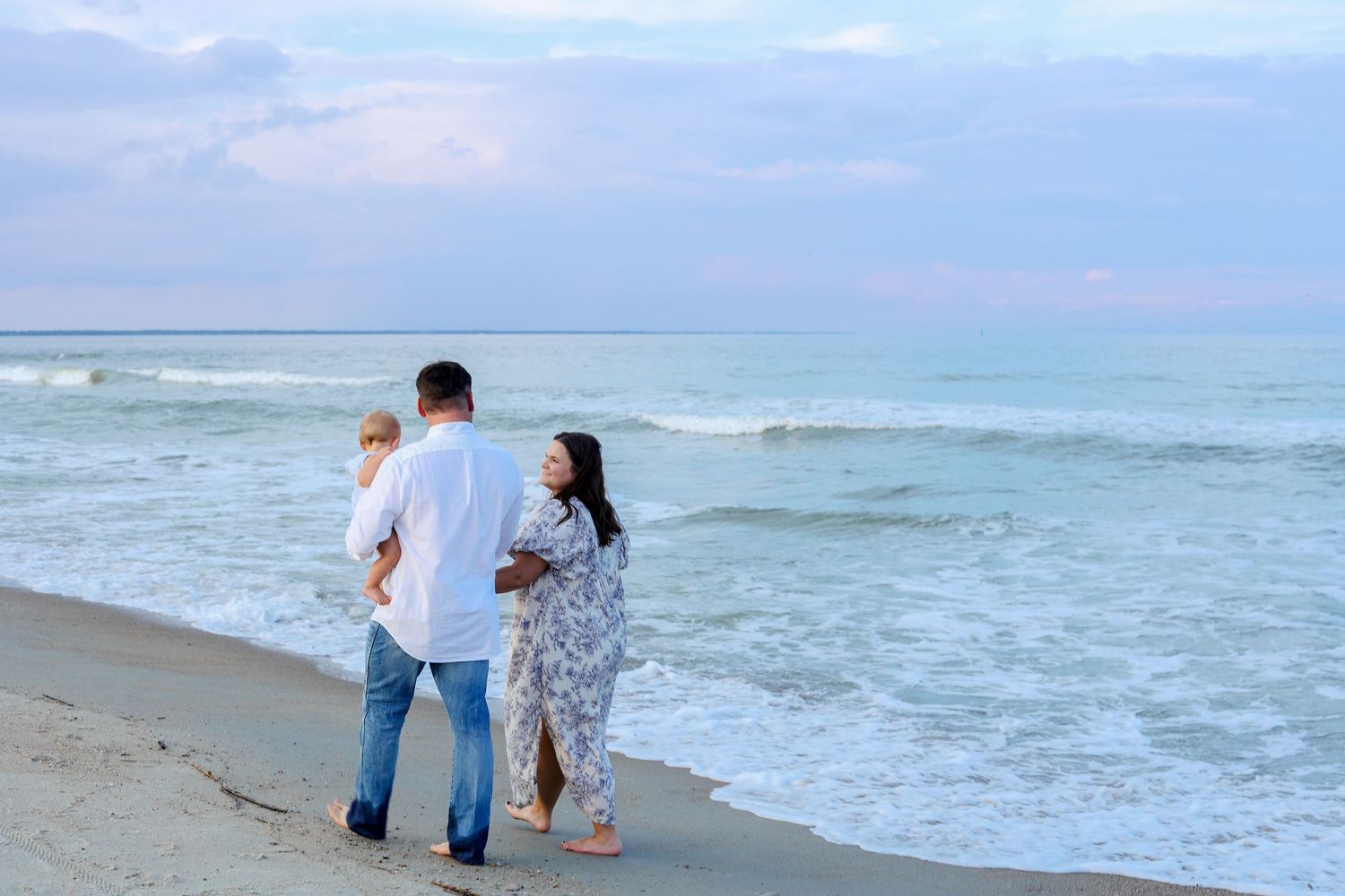 Multiple groups stroll along a peaceful beach with gentle waves and blue skies.