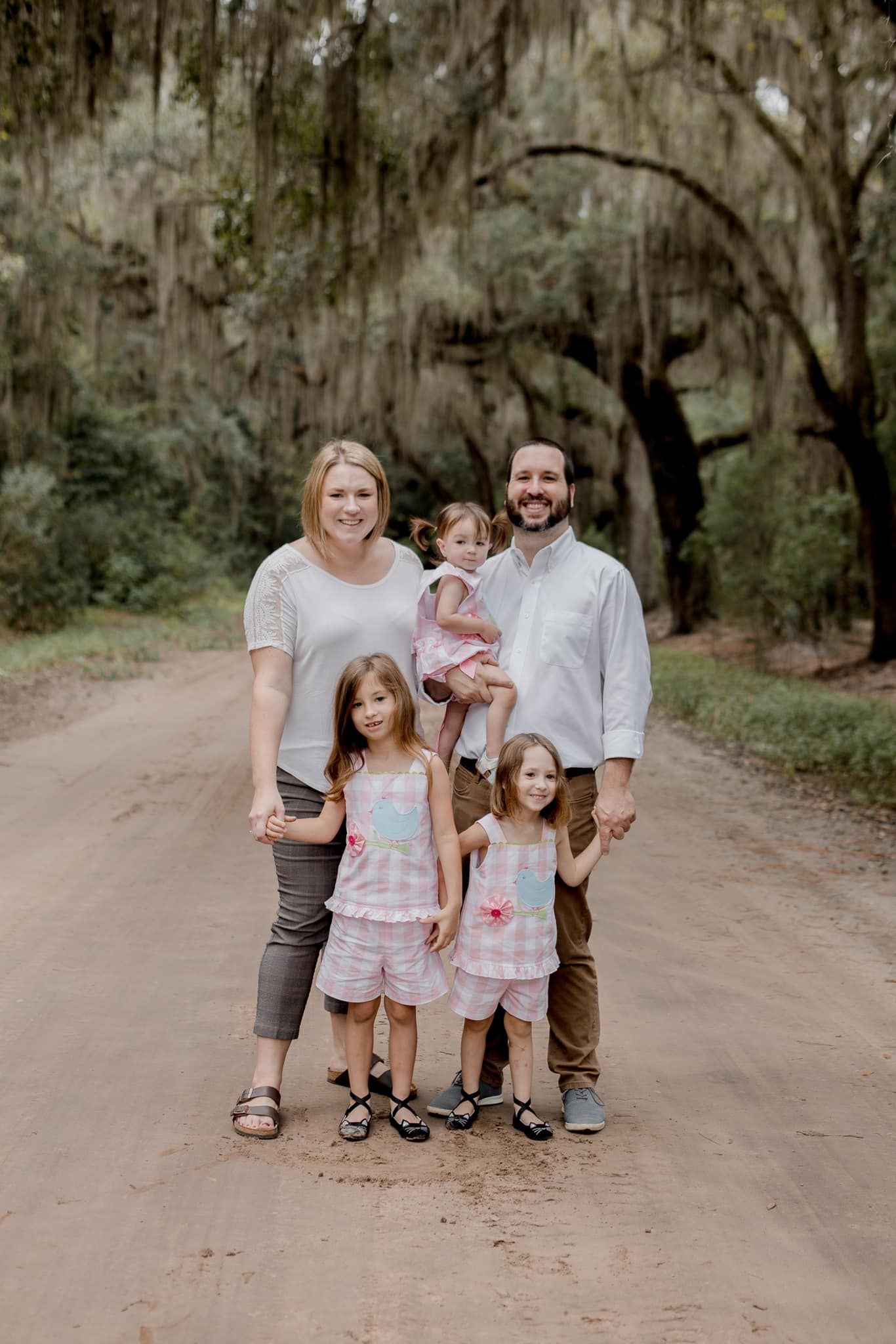 A family poses together on a dirt road lined with moss-draped oak trees.