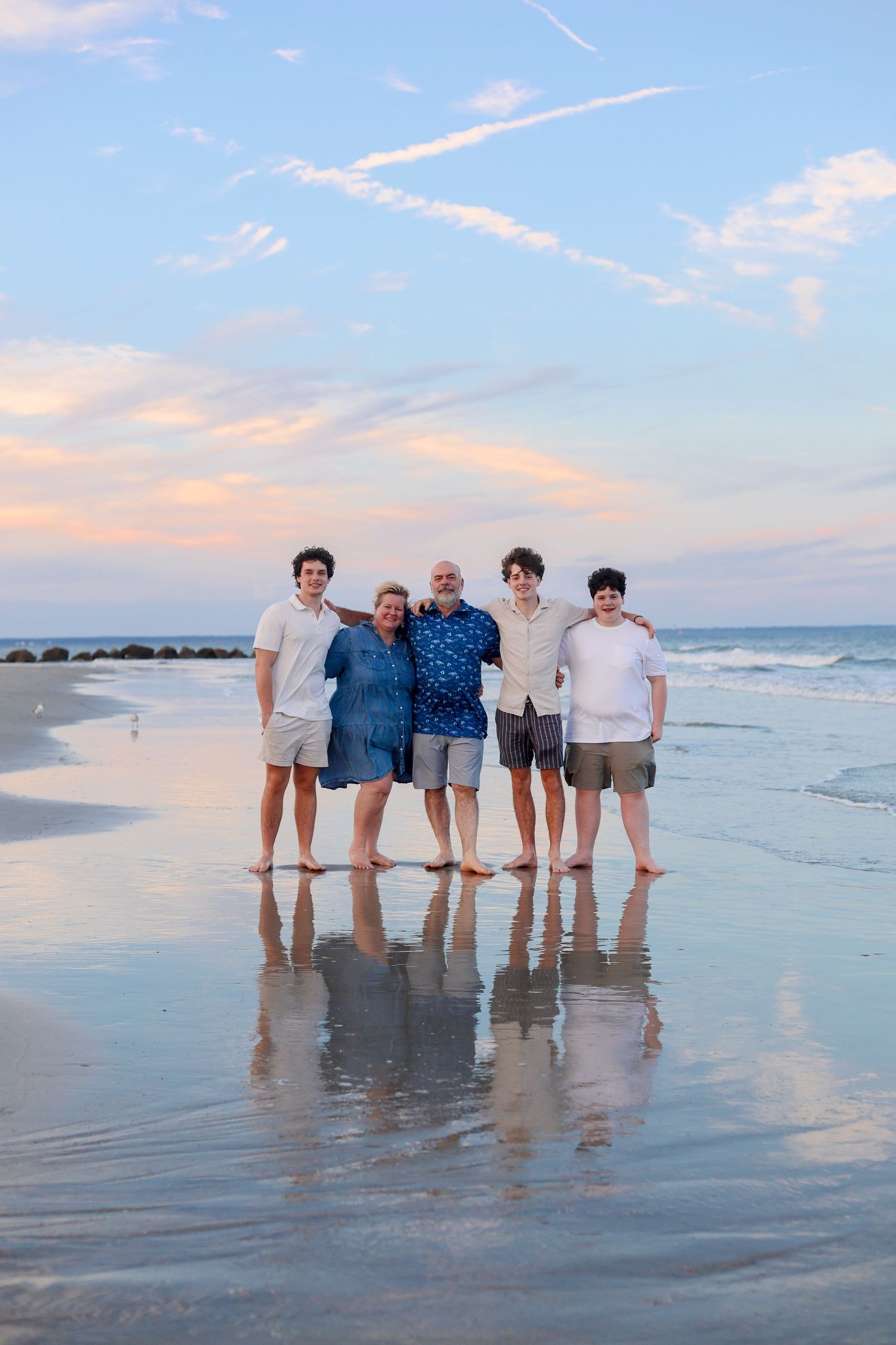 A group of people standing together at the beach during sunset with waves and sand visible in the background.