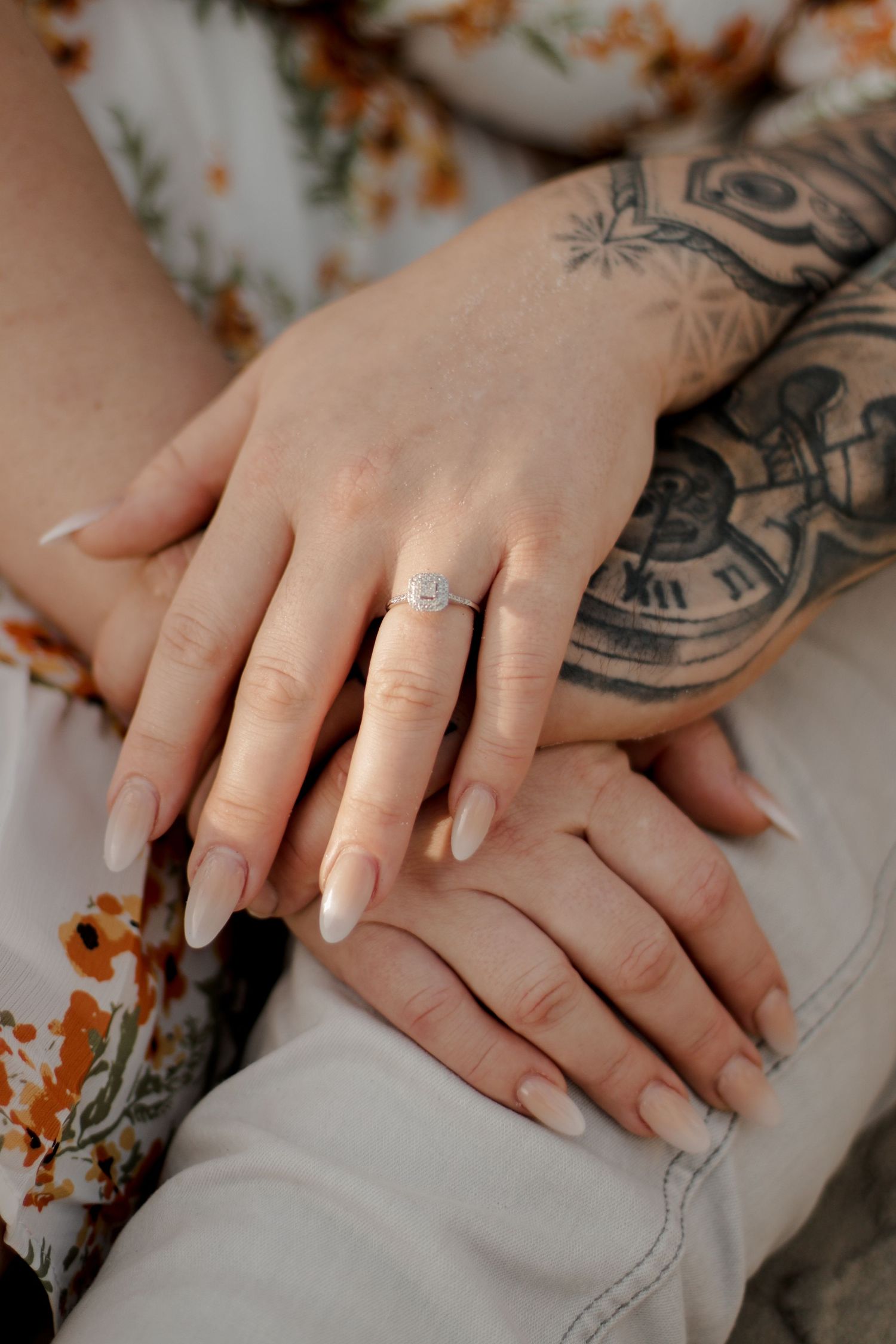 Close-up of engaged couple's hands showing diamond ring and tattoos.