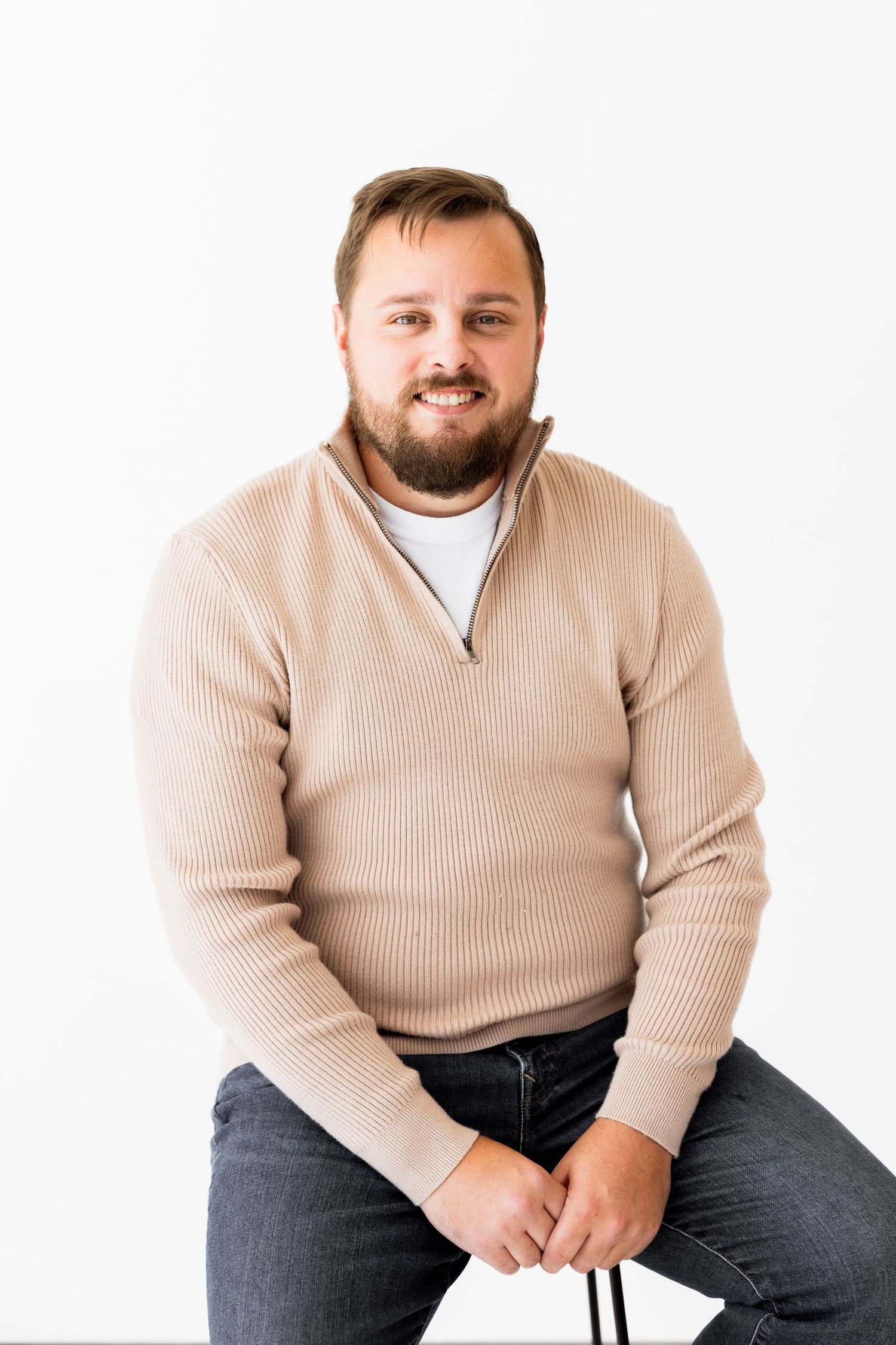Person in beige ribbed sweater and jeans sits casually against white background.