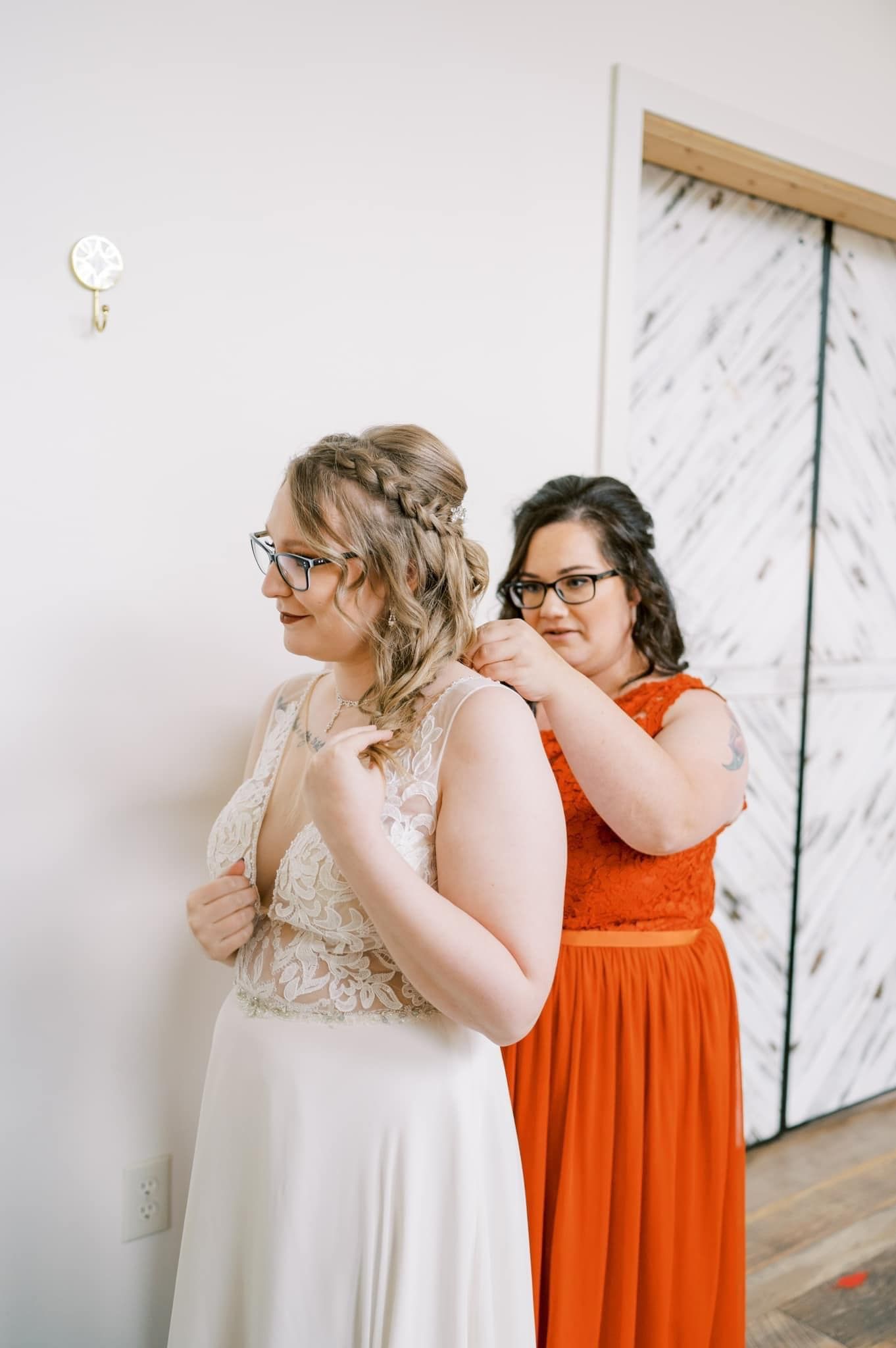 A wedding preparation scene showing a bridesmaid helping with the bride's dress.