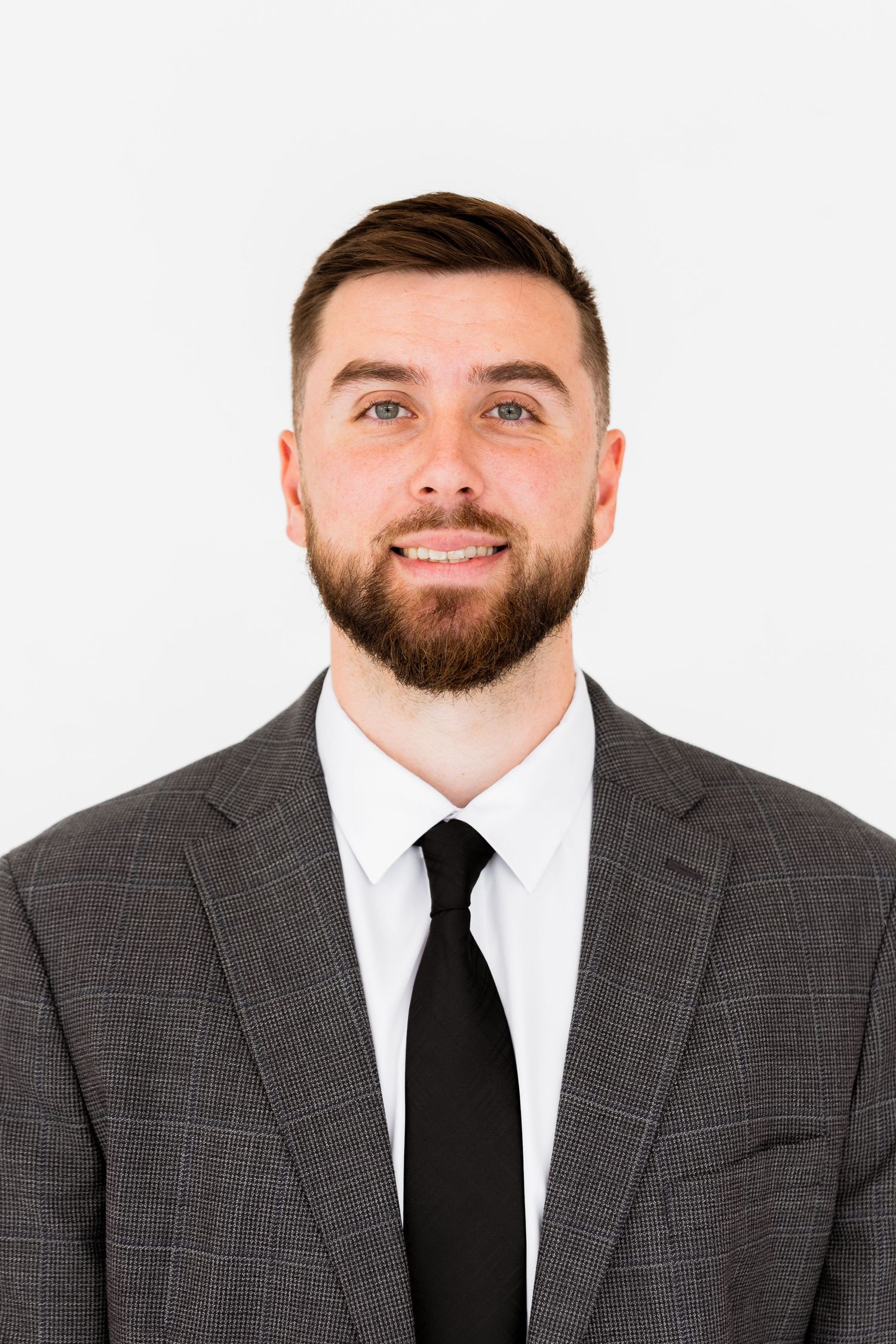 Professional headshot portrait of person in gray plaid suit and black tie smiling against white background.