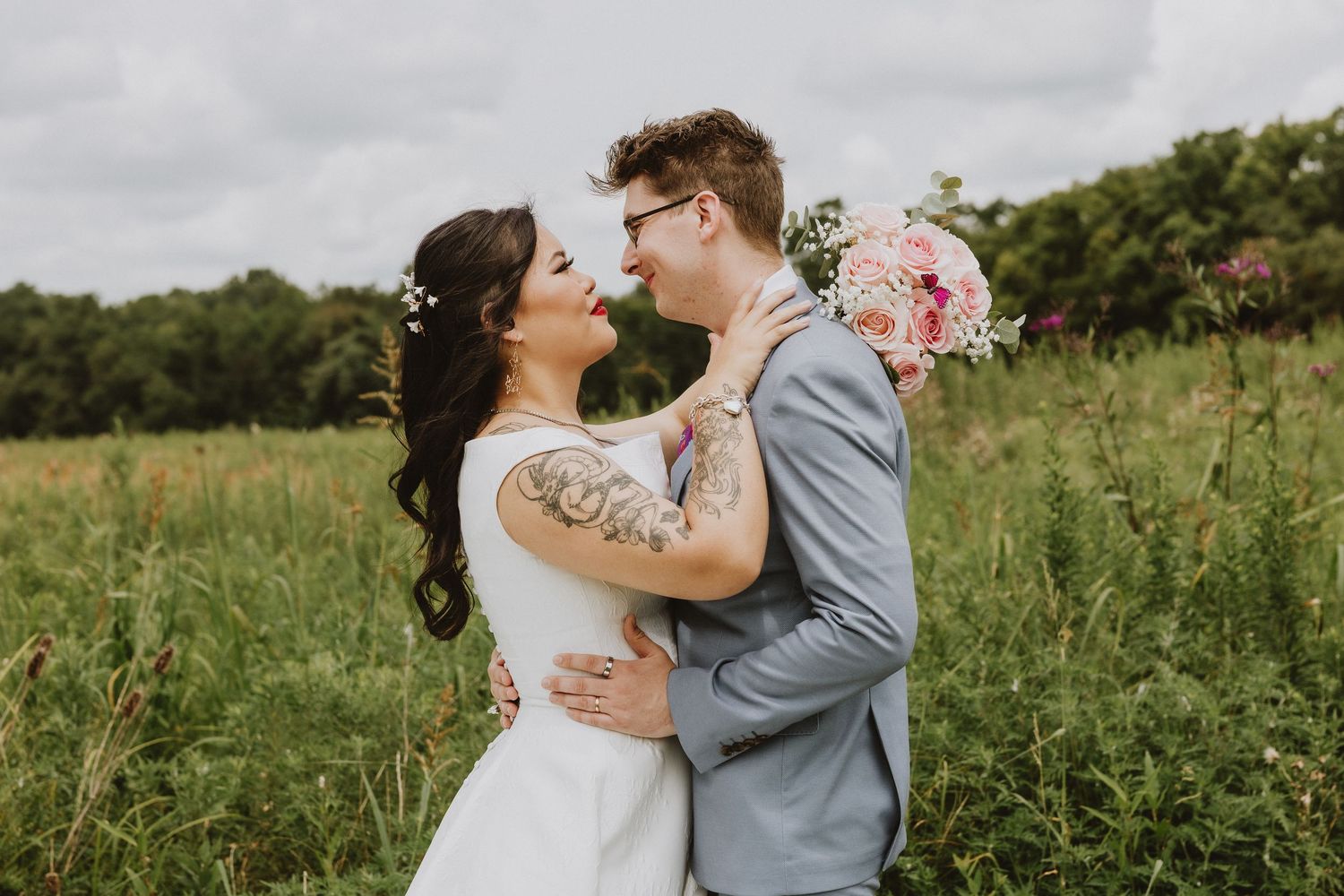 A romantic embrace between newlyweds in a summer meadow with natural scenery.