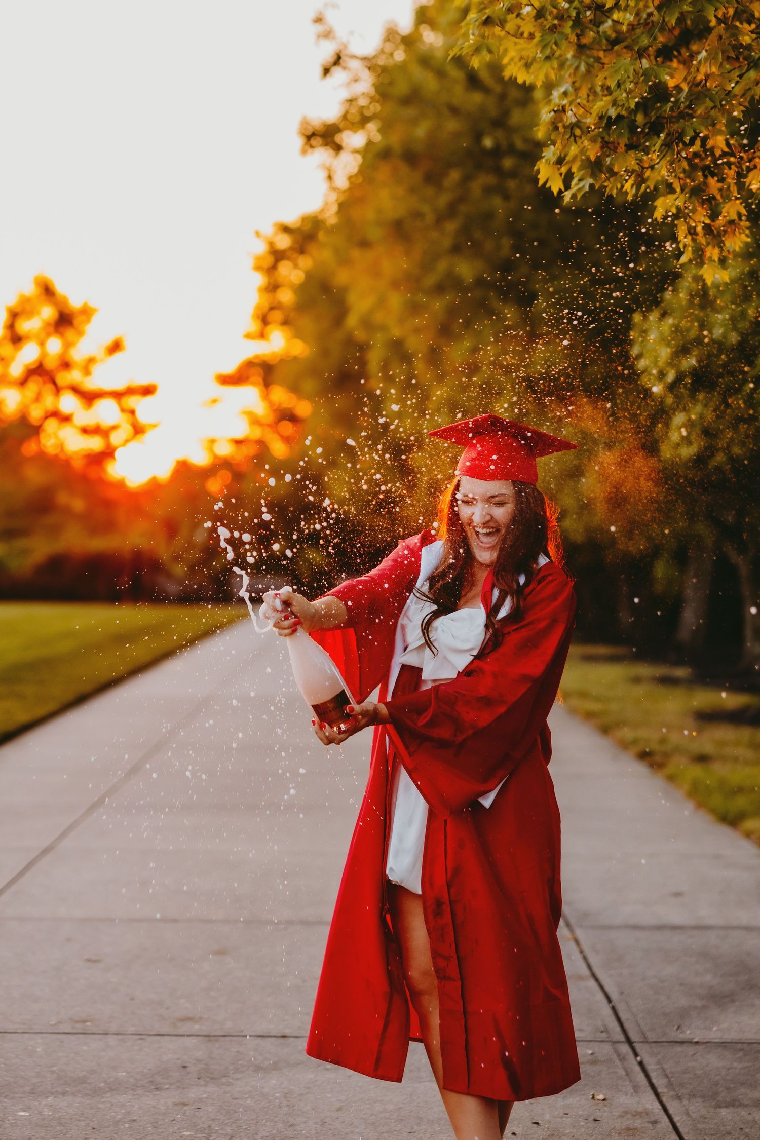 A figure in a bright red coat dances joyfully in an autumn park path at sunset as golden light filters through trees.