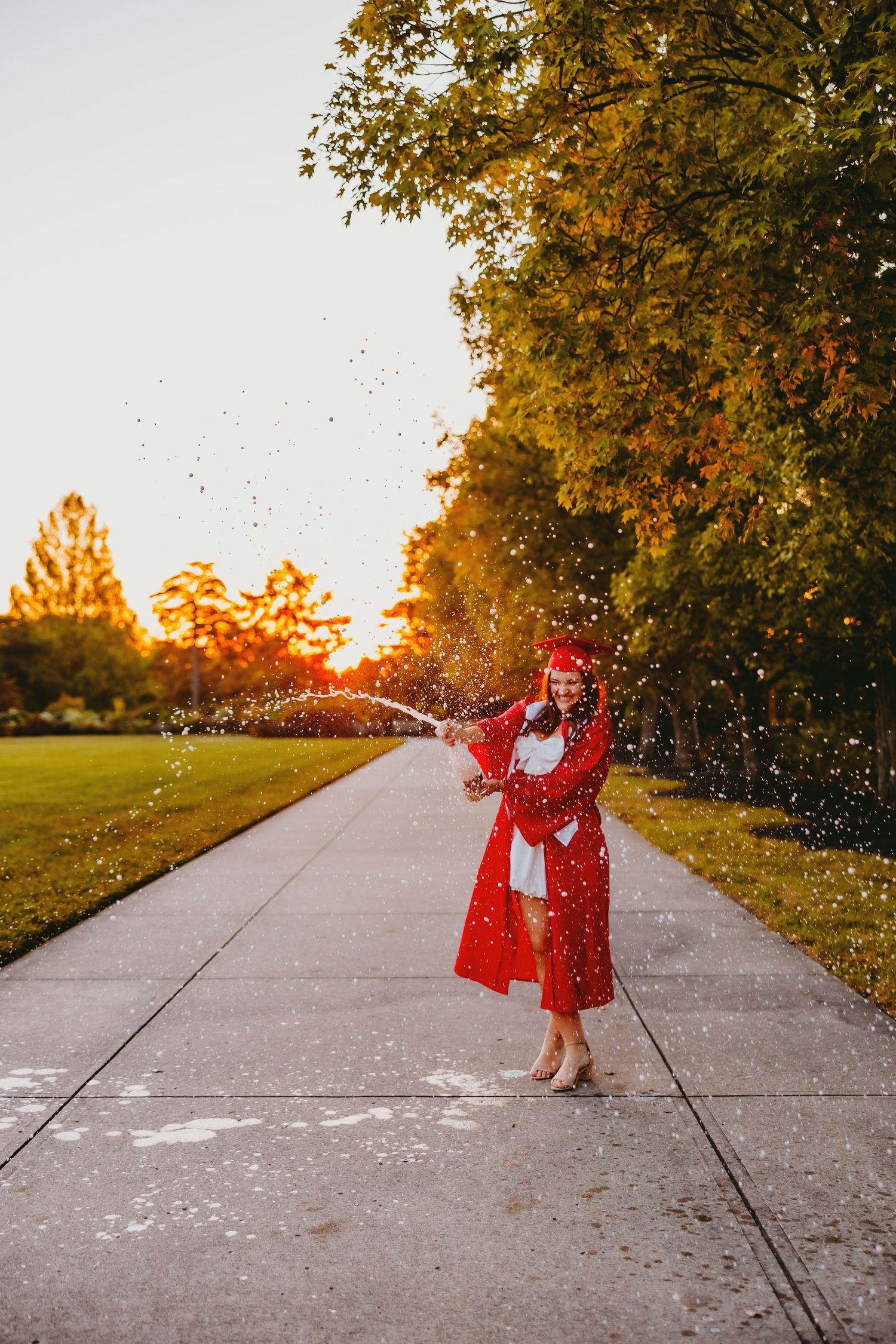 A figure in a red dress twirls and dances on a concrete path during golden hour as autumn leaves fall around them.