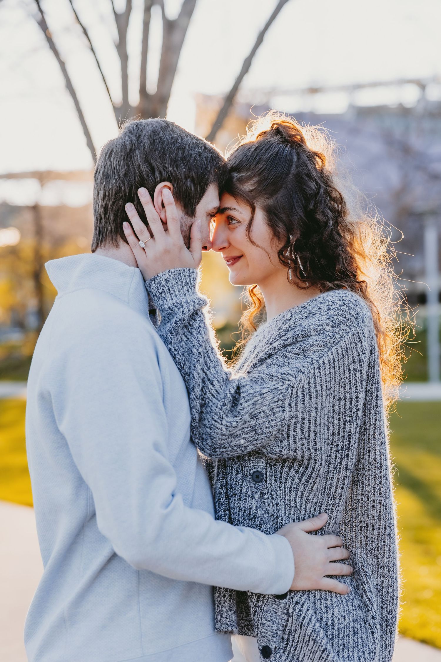 A romantic couple embraces outdoors at golden hour, touching foreheads tenderly in a warm autumn park setting.