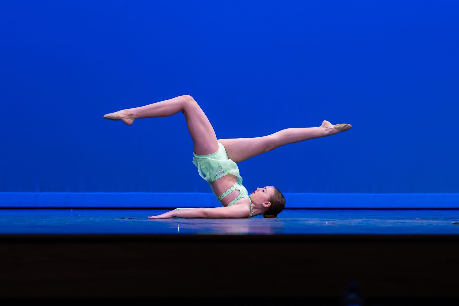 A dancer performs a graceful floor routine in a light blue leotard against a vibrant blue backdrop.