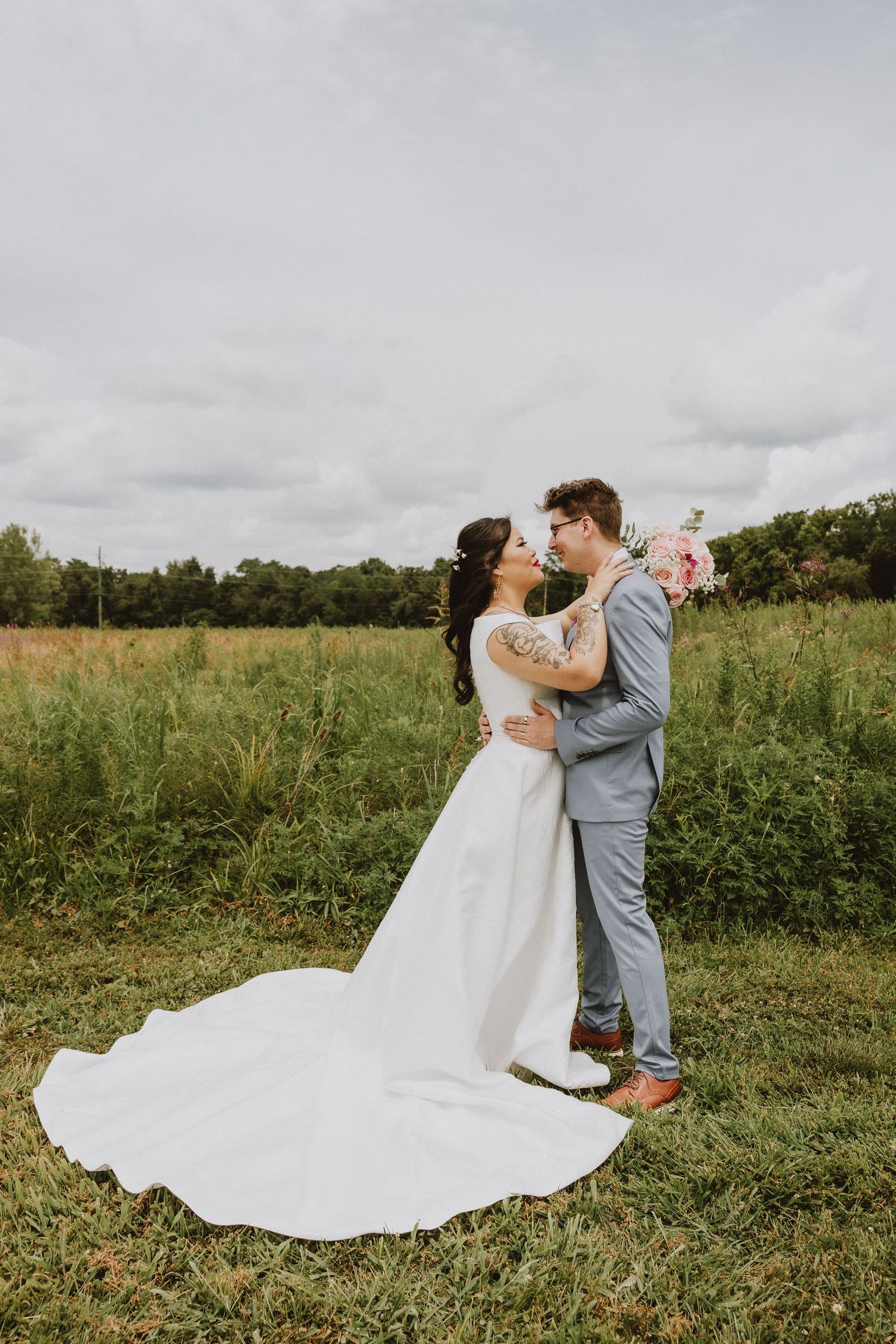 A tender wedding moment captured in a sun-drenched field with flowing white dress.