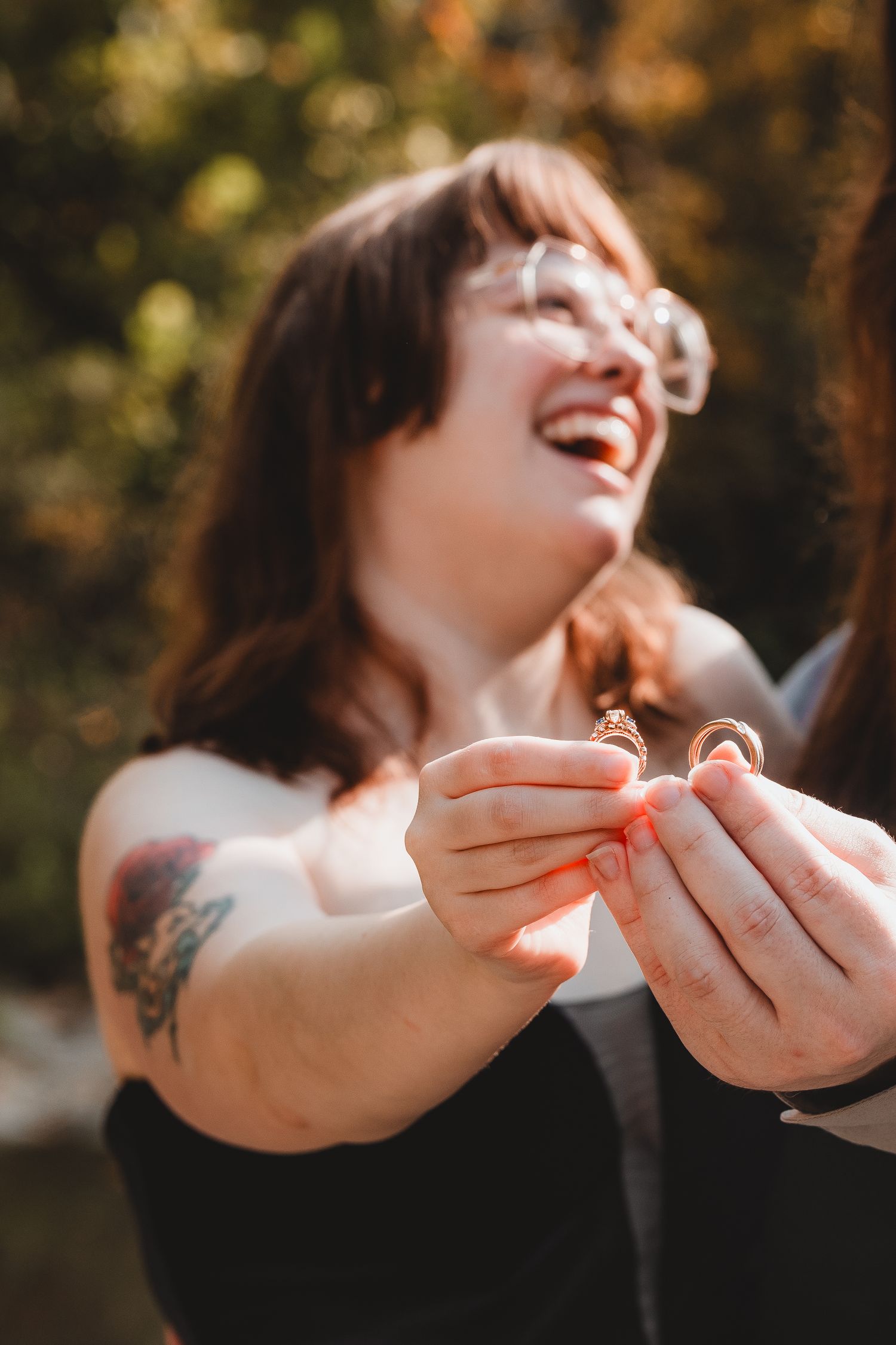 A joyful moment captured in warm sunlight as someone wearing black holds something small in their tattooed hands.