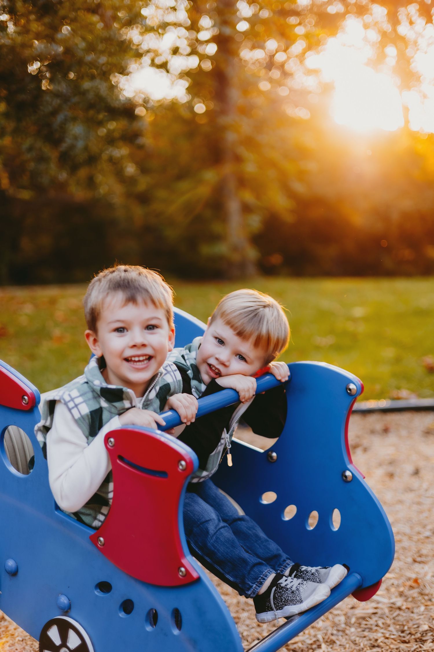 Two happy young boys playing on a blue playground ride at sunset in a park.