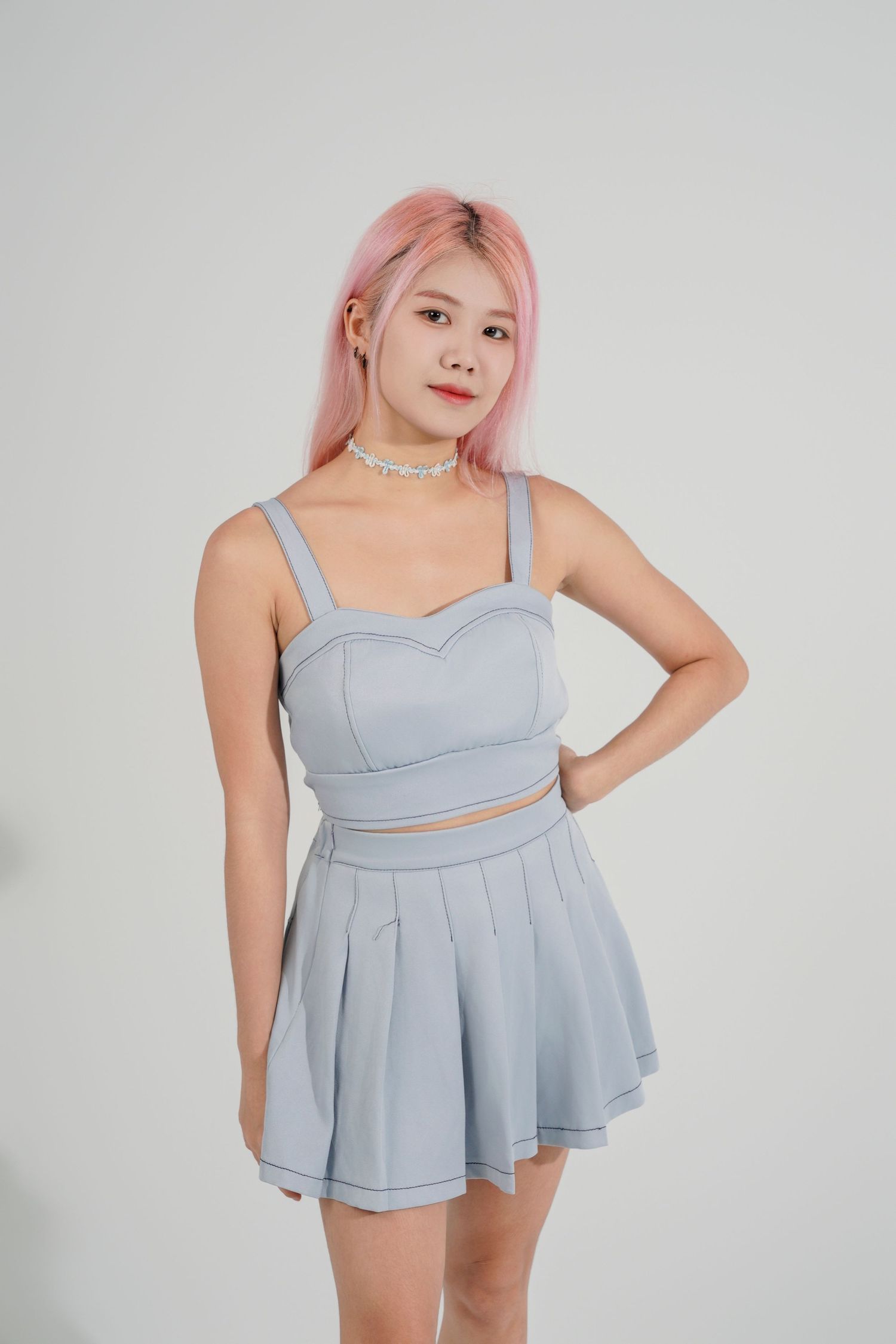 A model wearing a light blue two-piece swimsuit with pleated skirt detail poses against a white studio background.
