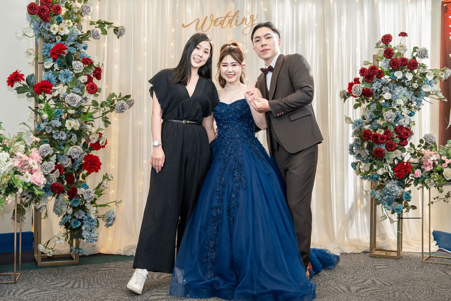 A romantic wedding celebration with blue gowns and red rose floral arrangements against a light curtained backdrop.