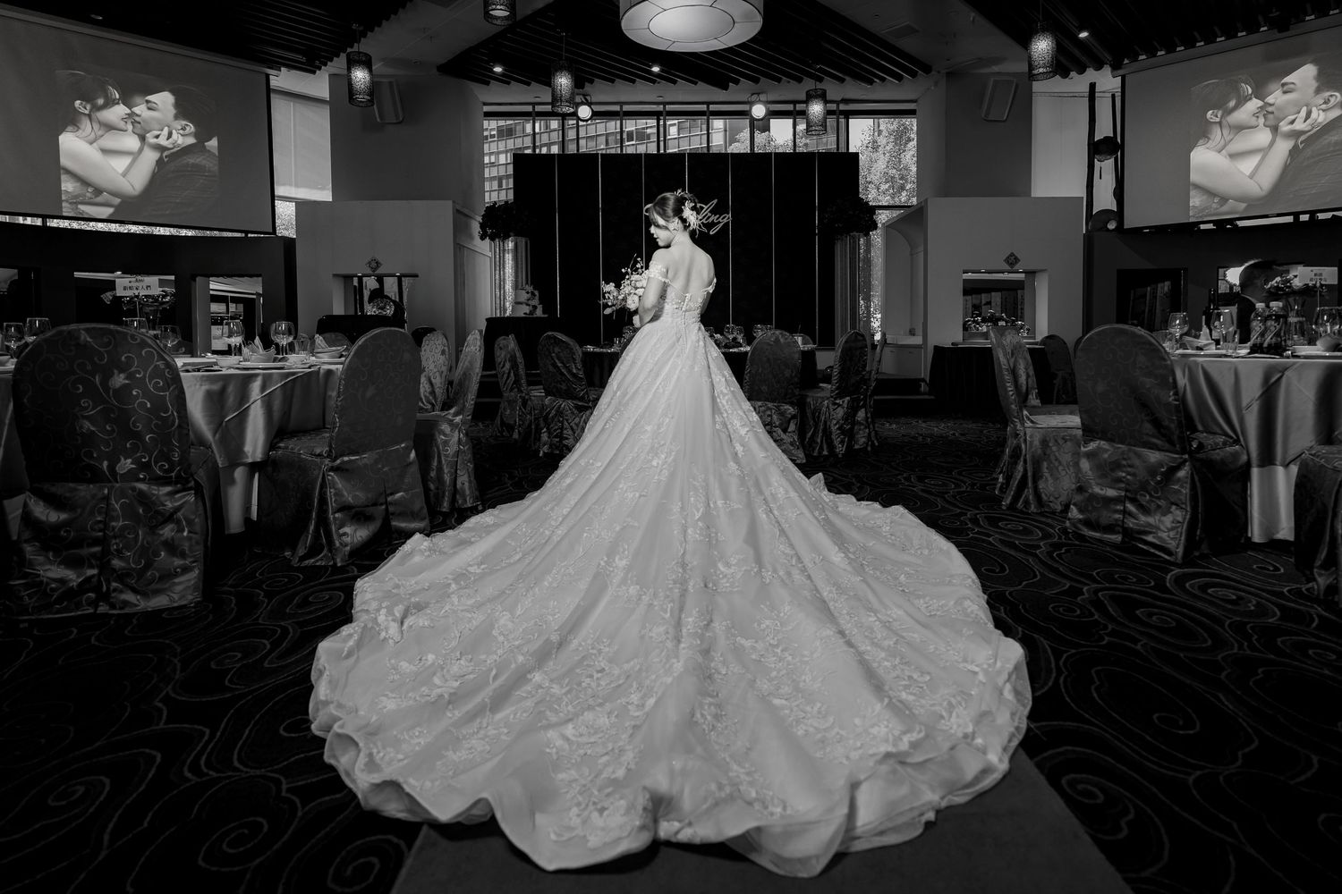 A stunning wedding gown with an elaborate cathedral-length train is displayed in a dimly lit reception venue.