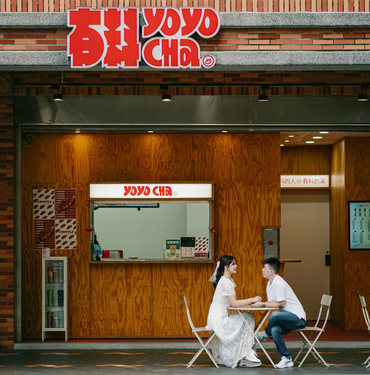 People sitting at tables outside a retro-style diner with red signage and brick walls in an urban setting.