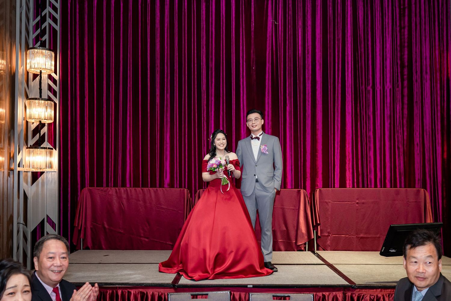 Performers take a bow on stage after a show with red curtains and stage lighting in the background.