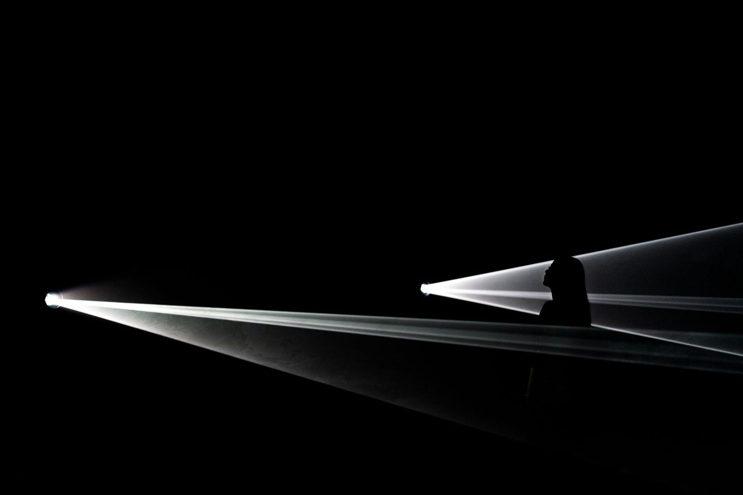 Dramatic light beams streak across a dark black background, creating a striking contrast in this minimalist abstract photography.