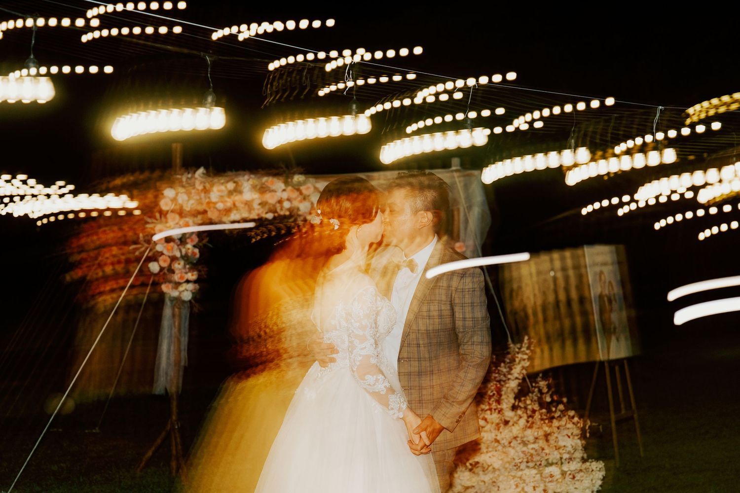 Motion blur captures dancers twirling on a dance floor with glowing lights creating streaks in the background.