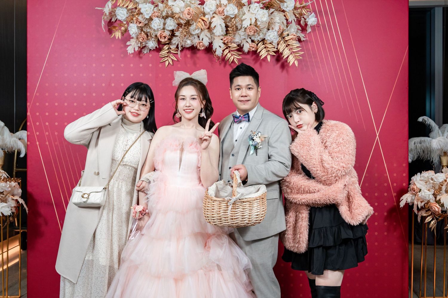 Wedding party poses in front of pink backdrop decorated with white cherry blossoms for formal portraits.