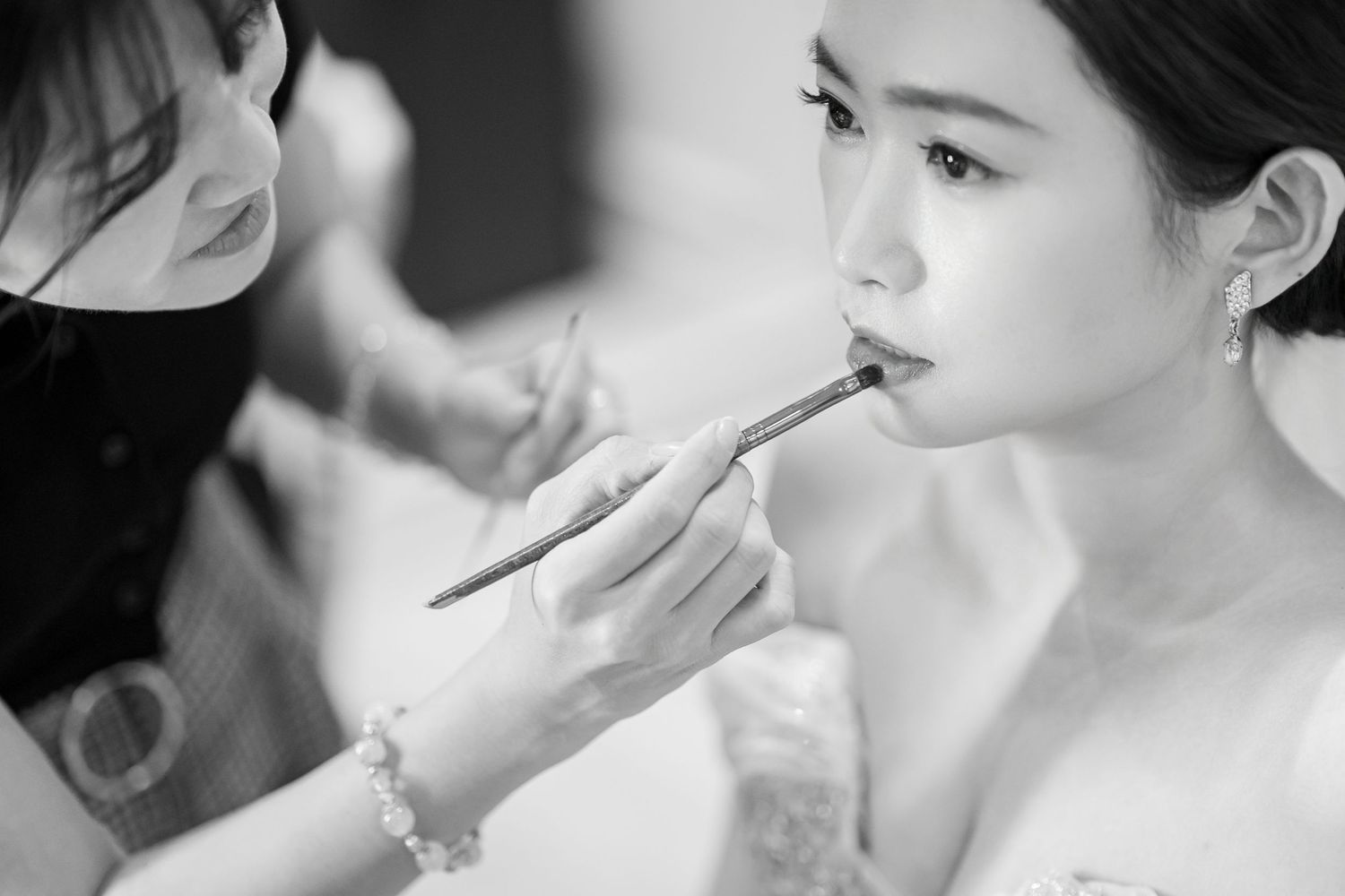 Black and white photo of a bride getting professional makeup applied during wedding preparations.