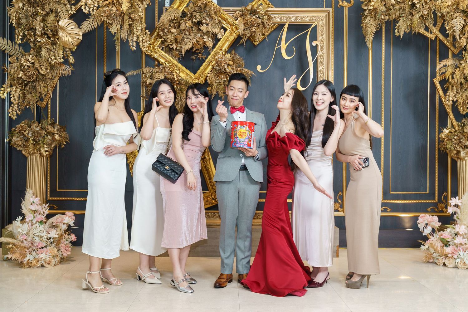 Wedding party posing in front of ornate gold-decorated blue wall at elegant celebration venue.
