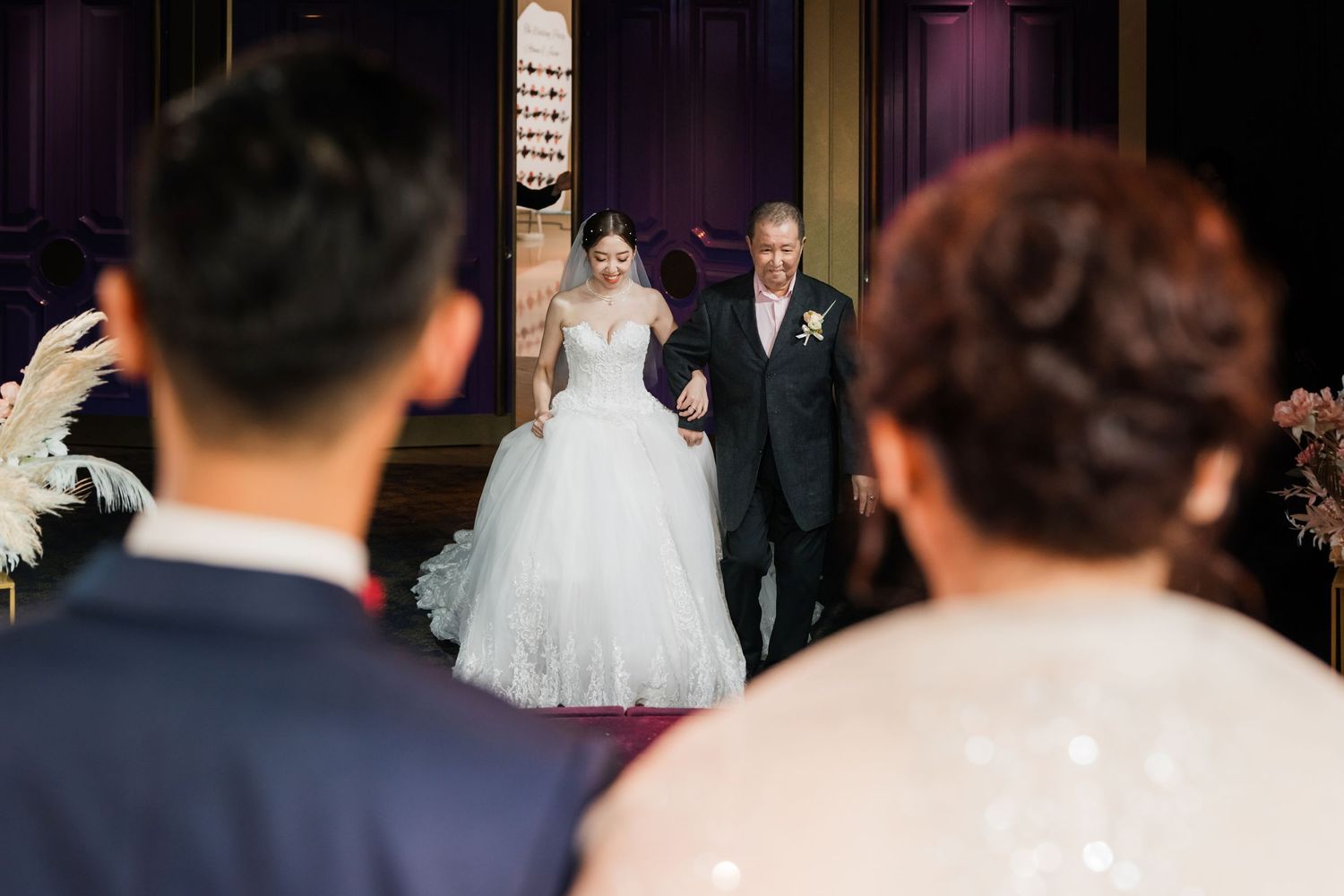 A wedding ceremony entrance captured from behind guests showing the couple at the doorway of an elegant venue.