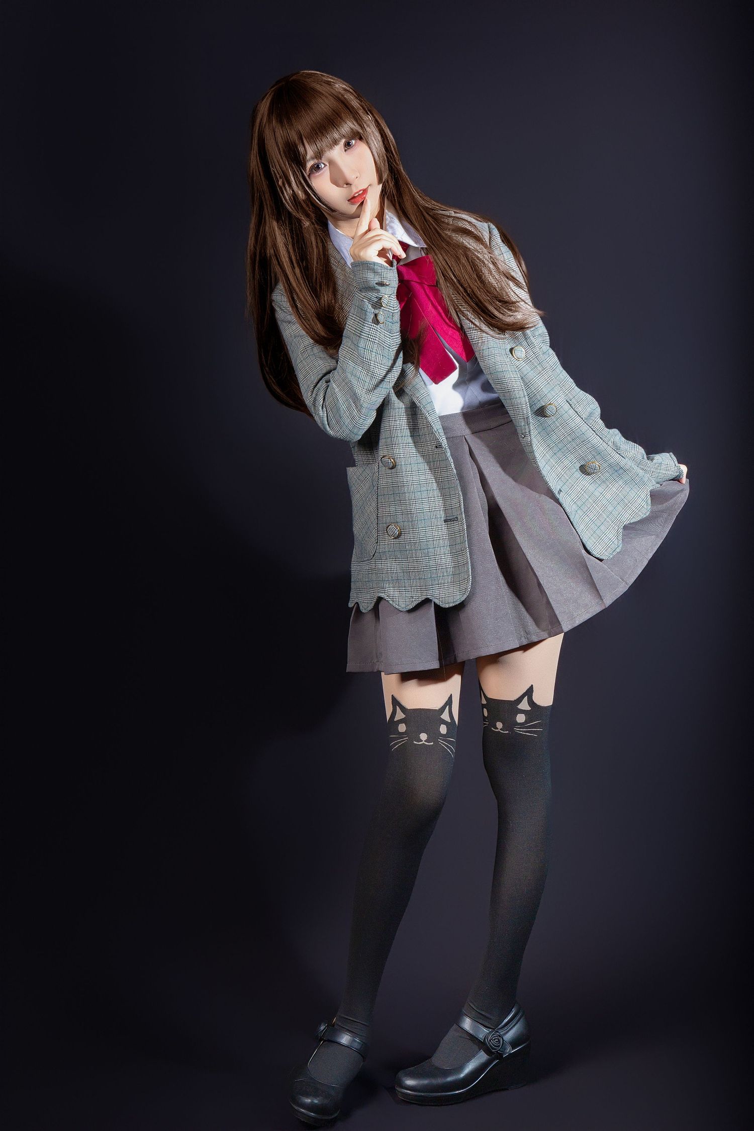 A cosplayer in a gray cardigan, pleated skirt and animal-themed knee socks poses against a dark backdrop.