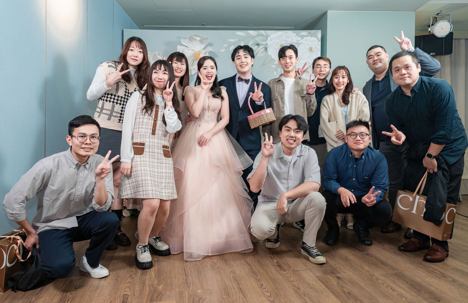 A group photo at a wedding celebration with guests posing together in a blue-walled room.