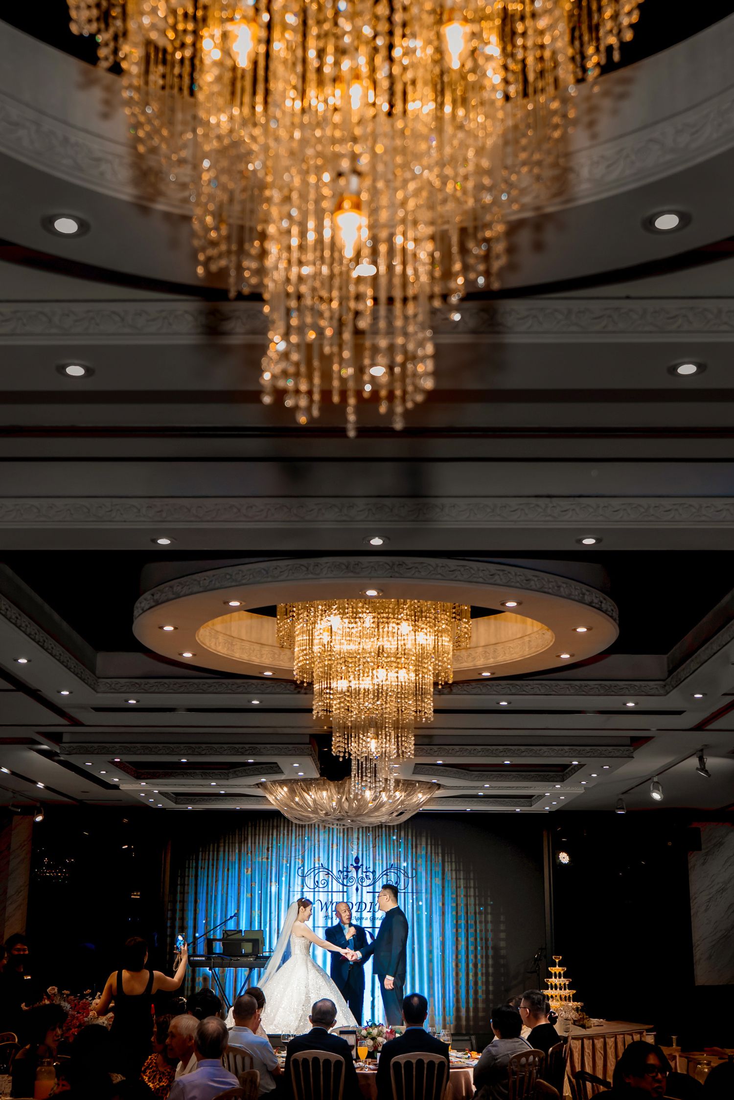 Elegant crystal chandeliers illuminate a wedding reception venue with cascading lights and dark ceiling details.
