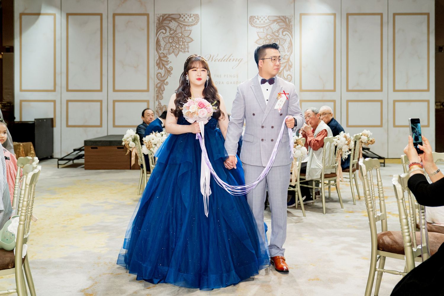 A couple in formal attire dances together in an elegant ballroom with gold-trimmed white walls.