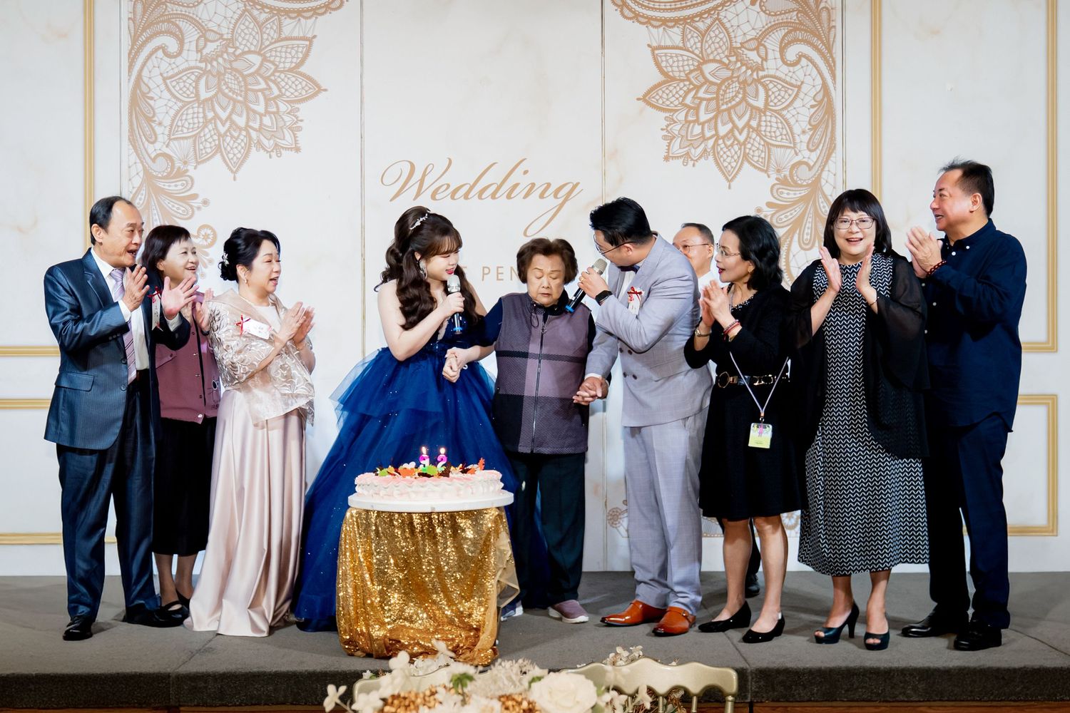 A group of wedding guests celebrate around a decorated table with a gold tablecloth at an elegant venue.
